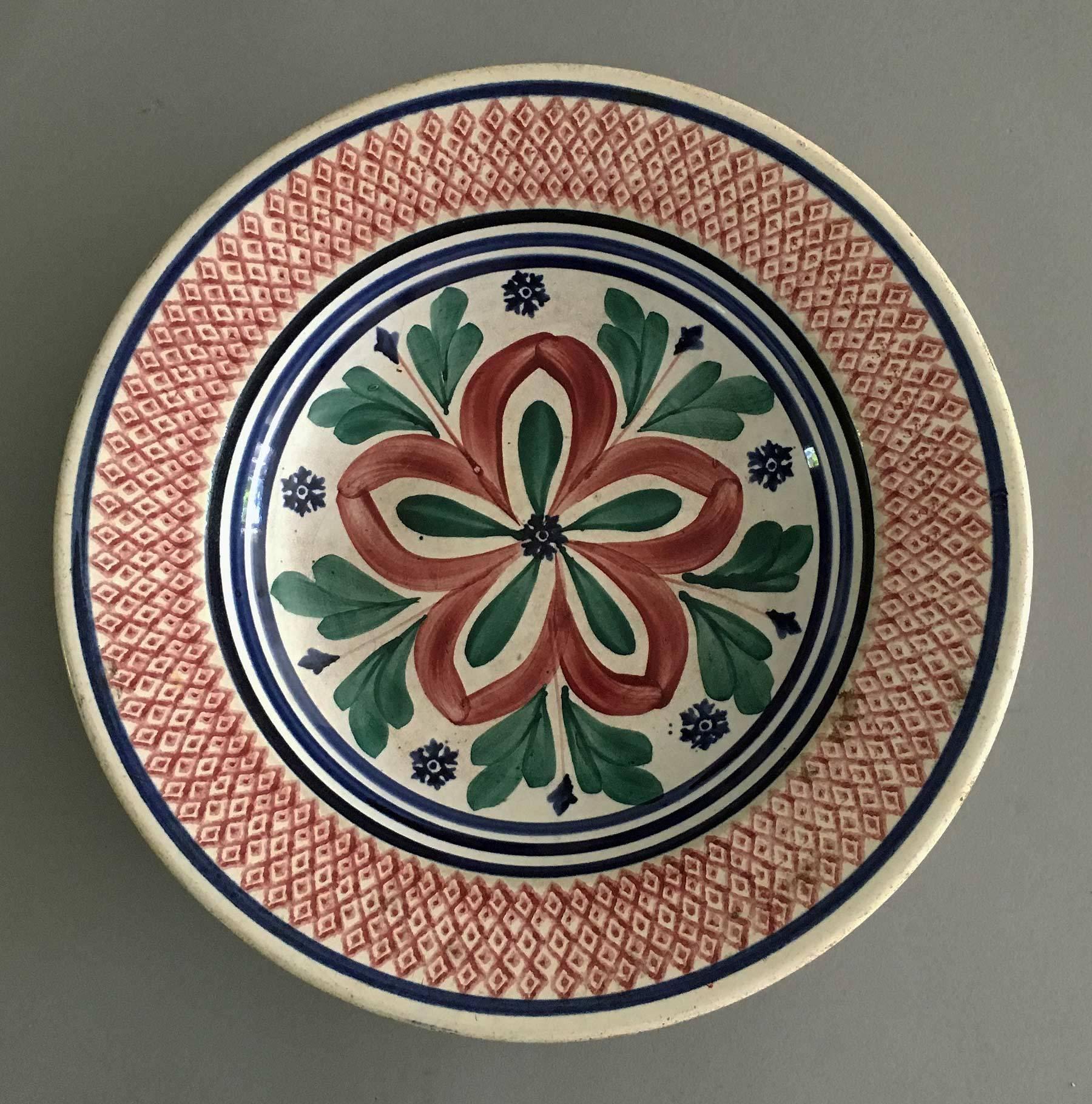 Matched set of four Dutch hand-painted pottery soup or pasta bowls boldly decorated with stylized star flowers in red, green foliage and tiny blue flowers, the wide rims decorated in a diamond diaper pattern, trimmed in blue. One of the backs is
