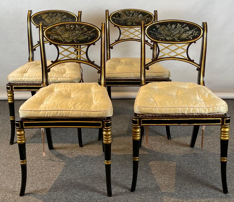 A set of four early 19th C. English Regency ebonized dining chairs with grisaille paint decorated crest rails and pierced splats accented with subtle red banding and gilt decoration all with cane seats and custom fitted loose cushions.
