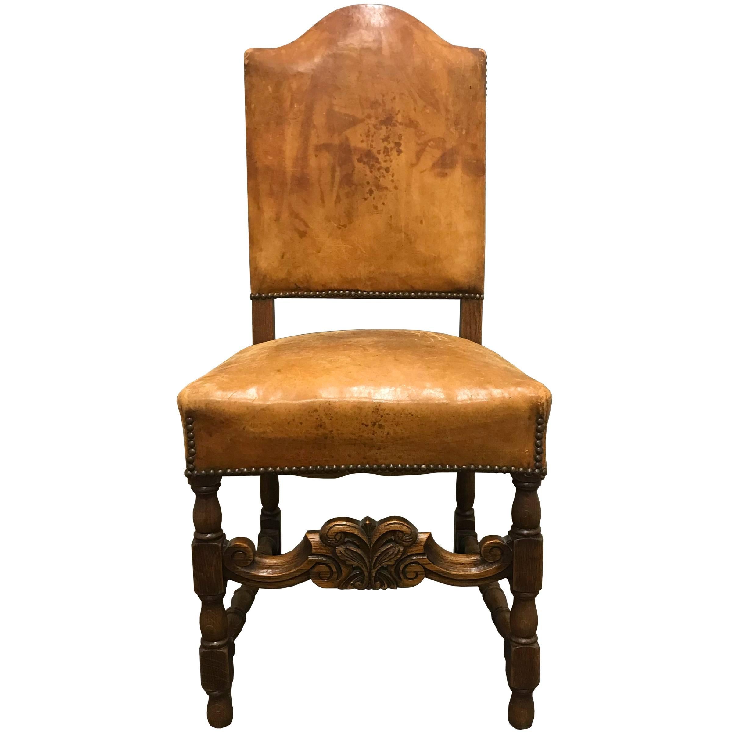 A set of four early 20th century Danish dining chairs with wonderfully worn leather upholstered seats and backs, floral carved stretchers, turned legs, and nailhead trim. Found in Denmark.