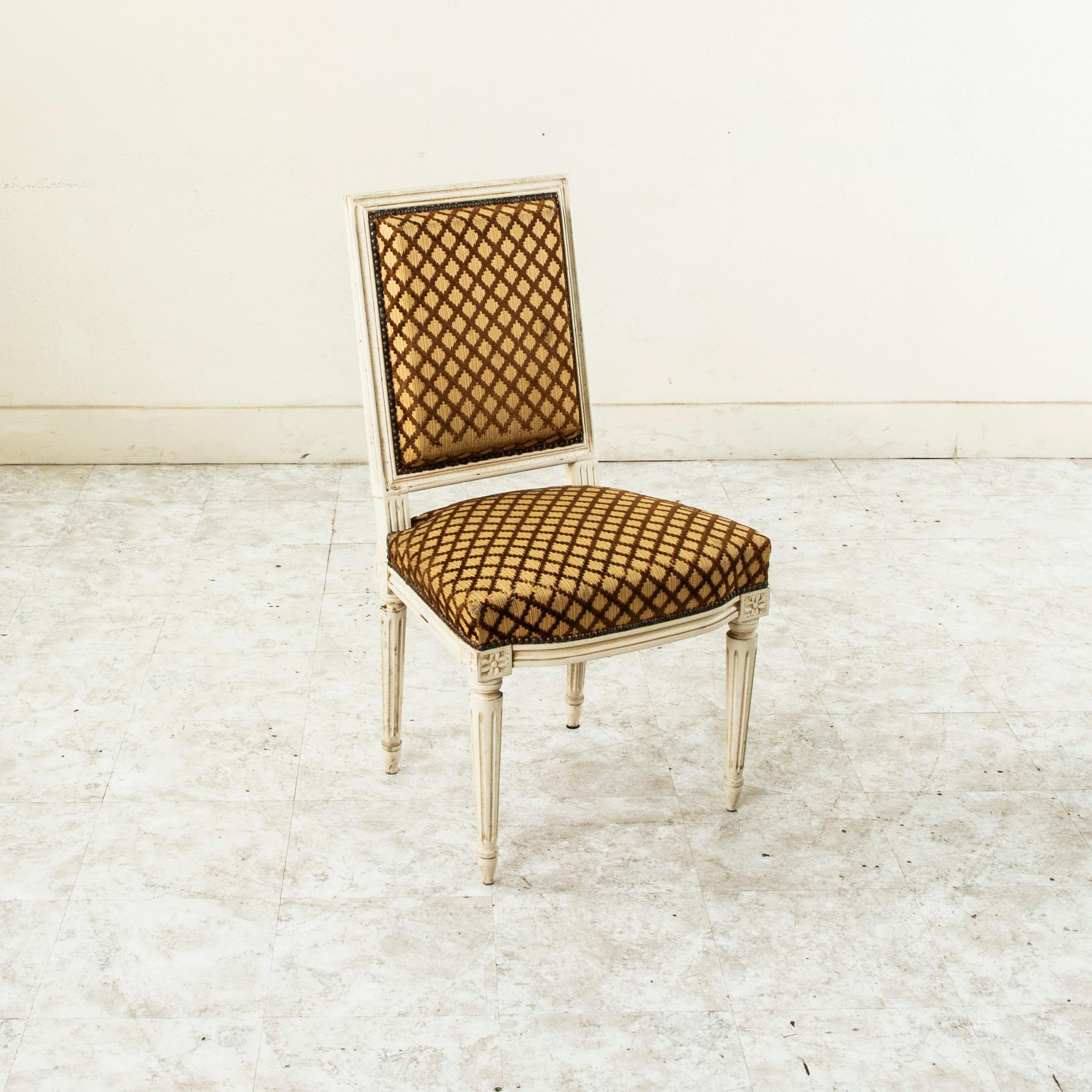 This set of four early twentieth century French dining chairs or side chairs is in the Louis XVI style and features carved rosettes on the die joints and classic tapered fluted legs. The frames are painted in an off white, and the seats and backs