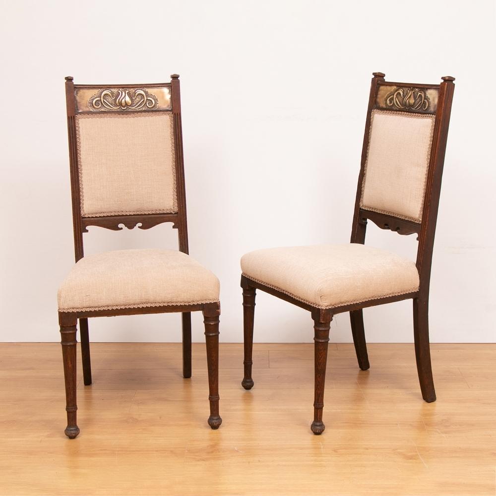 A set of four 20th century oak Arts & Crafts chairs with decorative brass inlay and newly upholstered.

Measures: H: 102cm, W: 46cm, D: 53cm, seat height: 48cm.