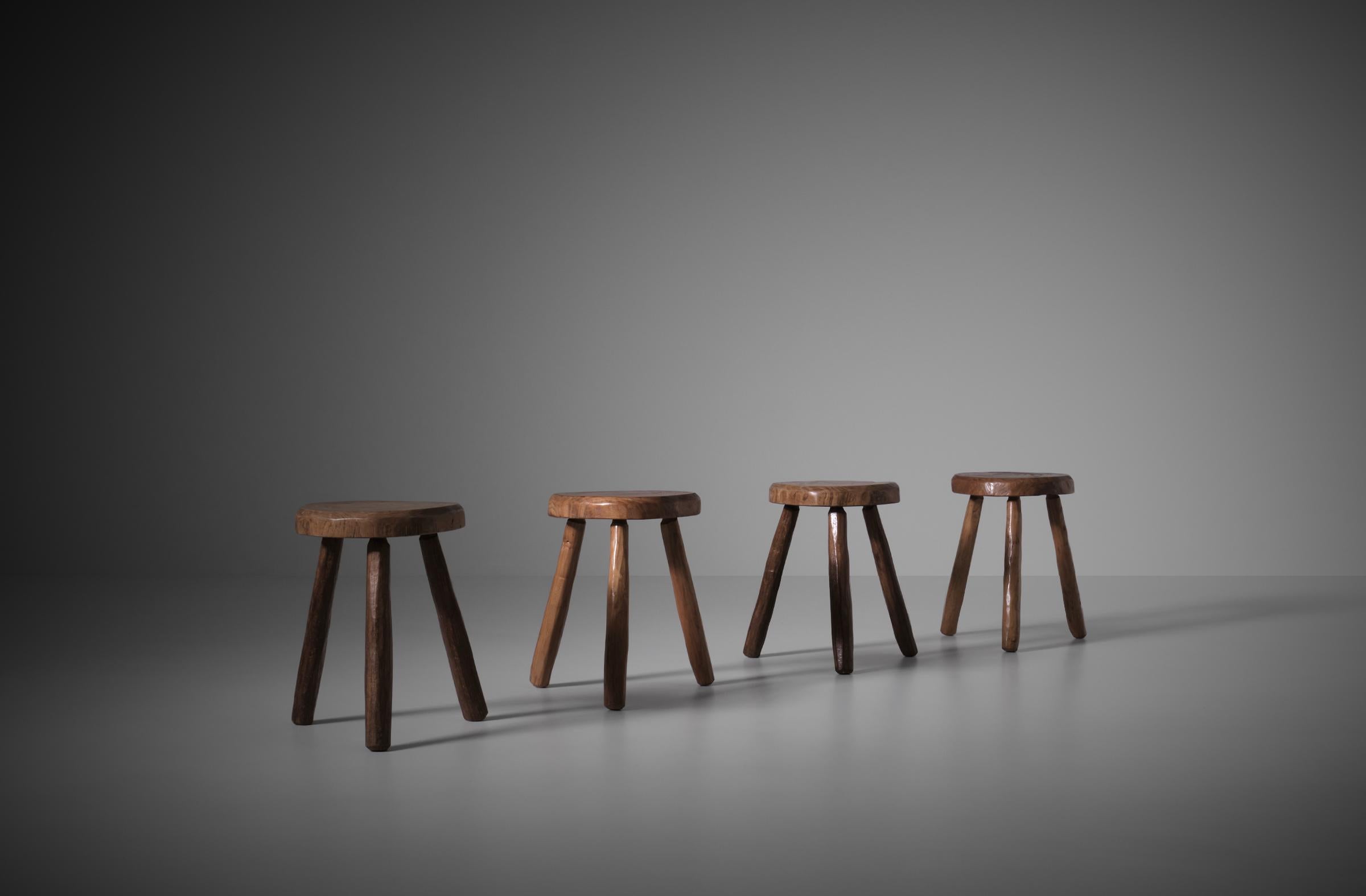 Set of four art populaire tripod stools in solid Elm, France 1960s. The seats of the stools are nicely shaped in a free round shape. The thick seats and sturdy feet make them very attractive and sculptural. Nice hand-crafted decorative pieces. The