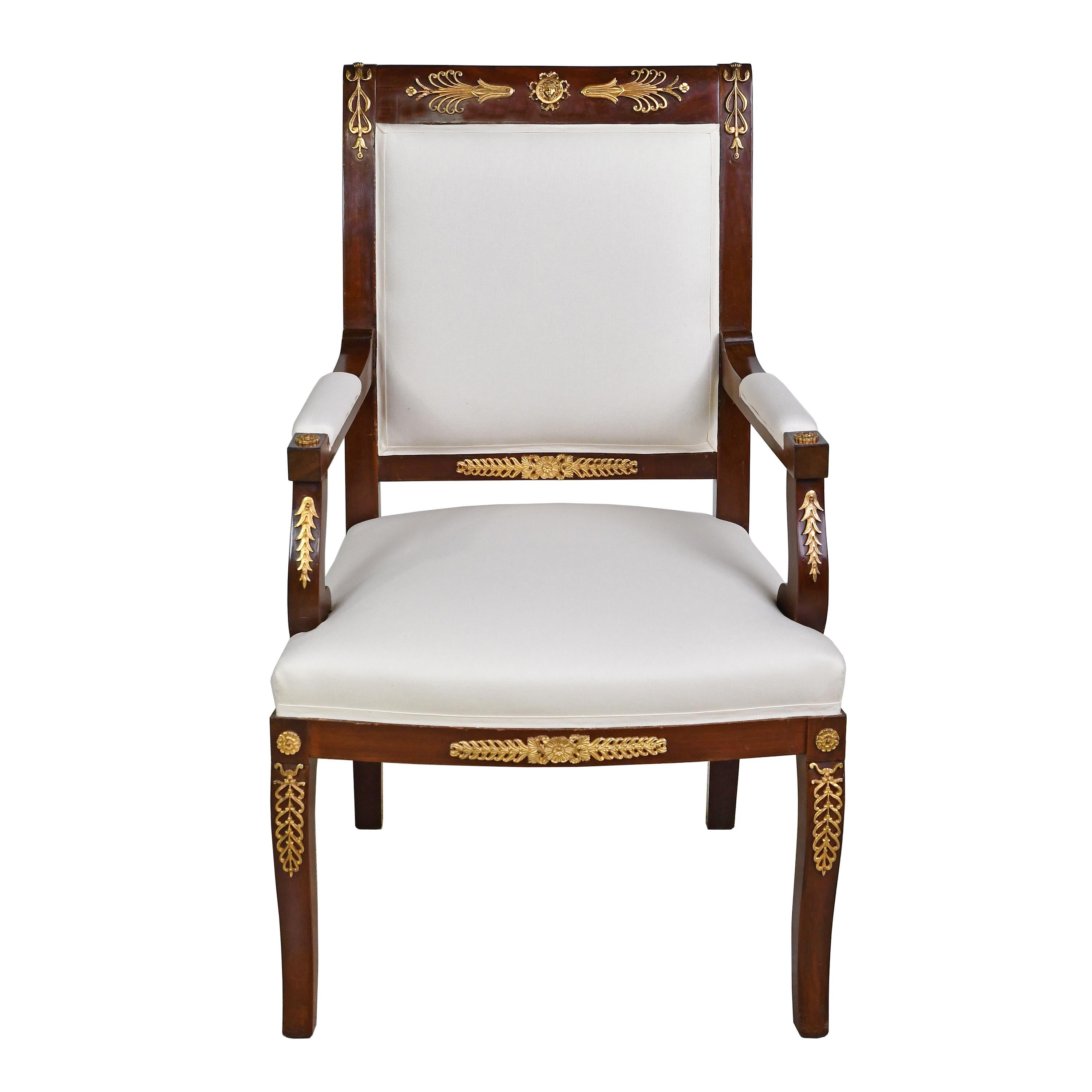 A handsome set of four Empire-style armchairs in a dark rich auburn brown mahogany with bronze doré ormolu mounts. Mounts embellish the frame with classical motifs that were popular during the French Empire like anthemion’s, palmettes, lotus flowers