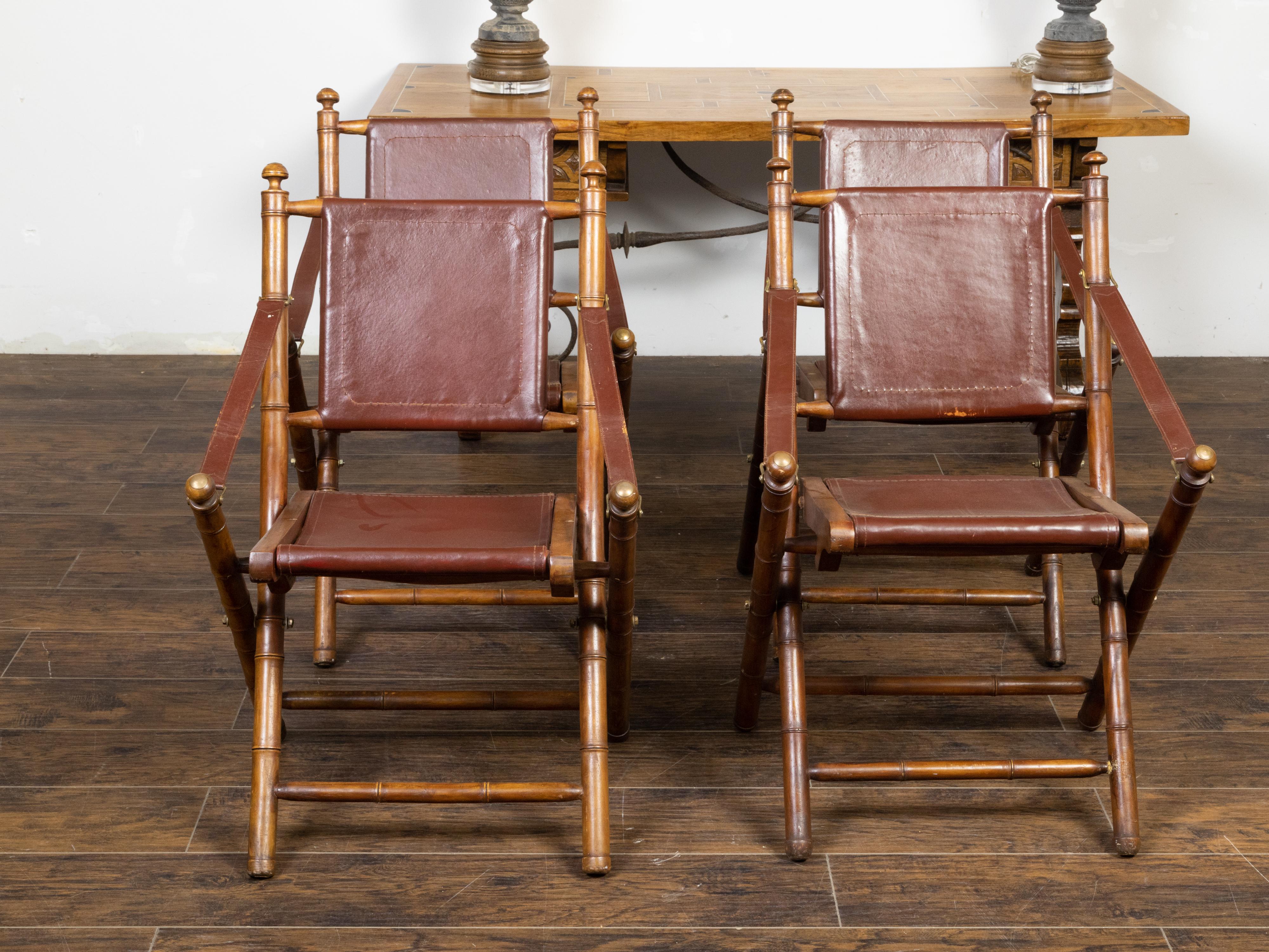 A vintage set of four English Campaign folding side chairs from the mid 20th century, with faux bamboo structure, leather seats and brass accents. Created in England during the mid-century period, each of this set of four Campaign chairs features a