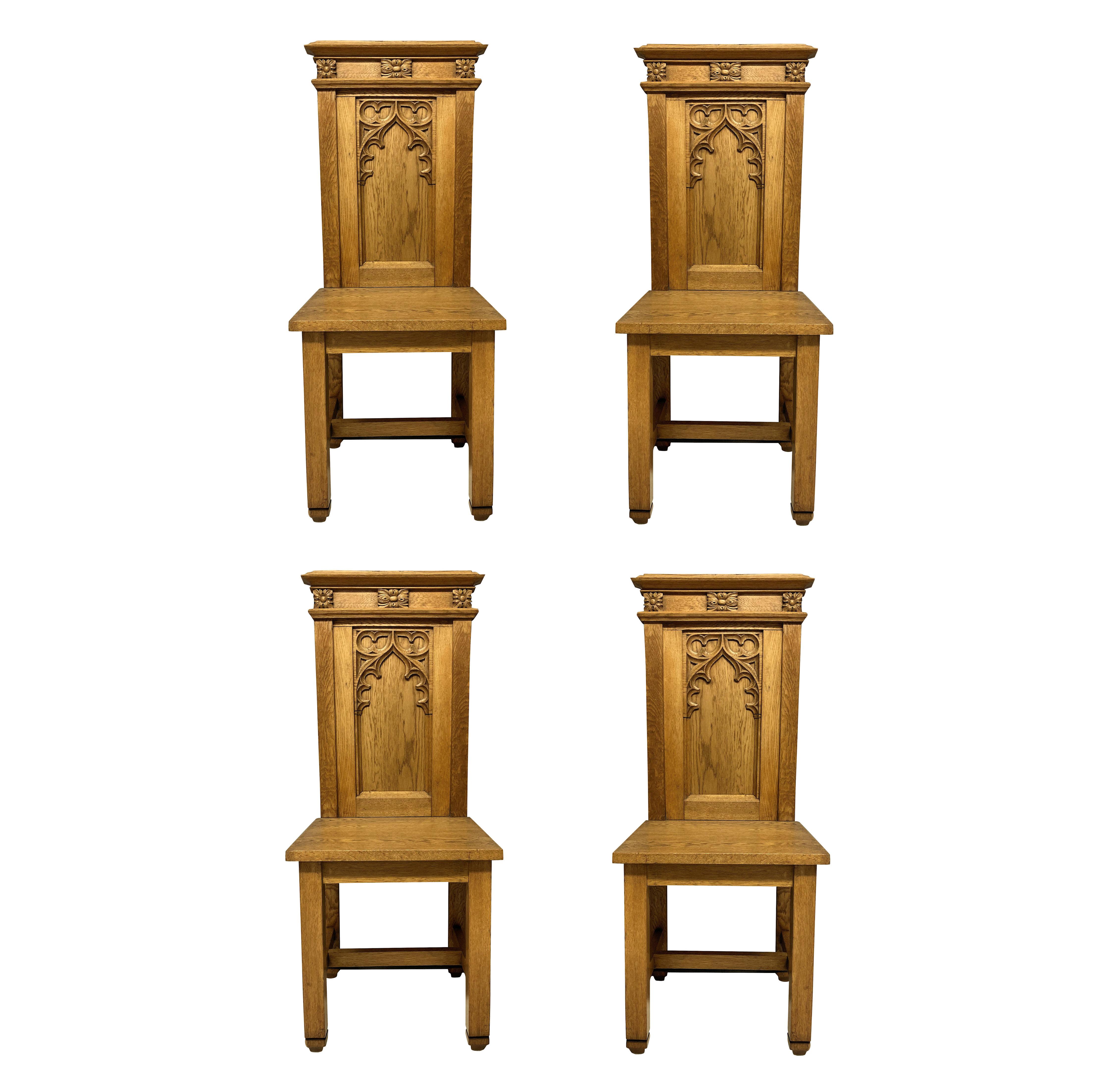 A set of four English pale oak Gothic hall chairs, with crisp carving.