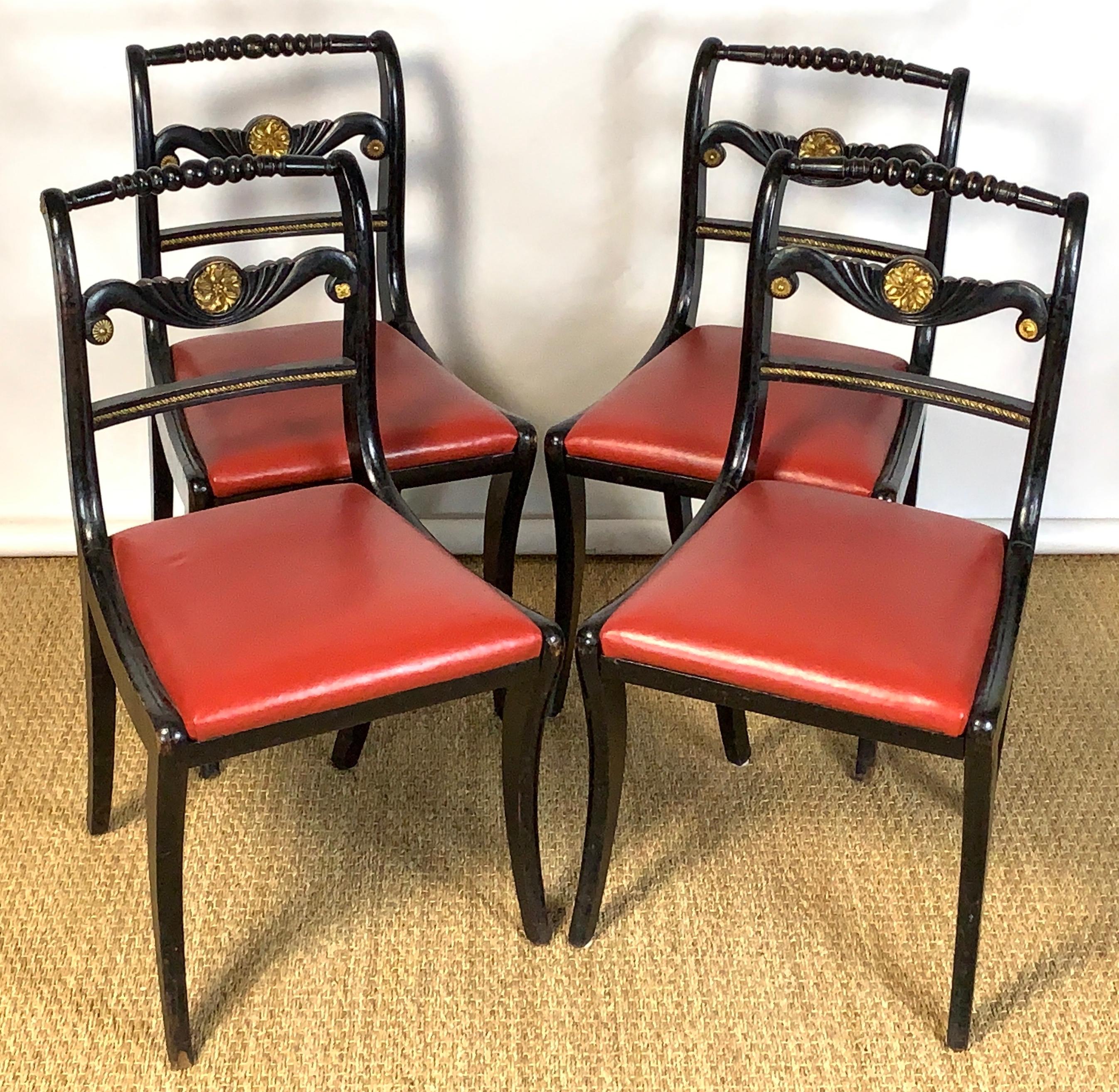 An elegant set of four ebonized English Regency period side chairs with carved giltwood accents recently upholstered with red leather seats.