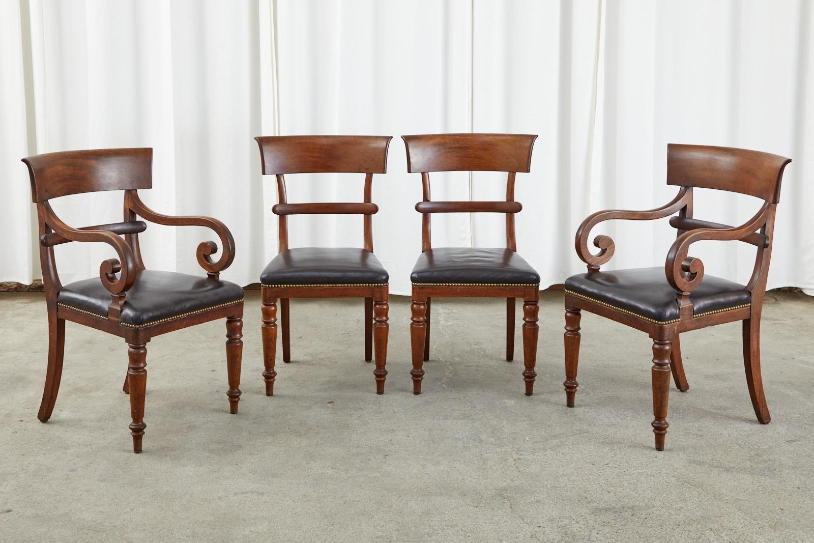 19th century set of English Regency dining chairs or library chairs crafted from mahogany. The set consists of two side chairs and two armchairs measuring 23 inches wide and 23 inches deep. The chairs have a klismos style tablet backrest with