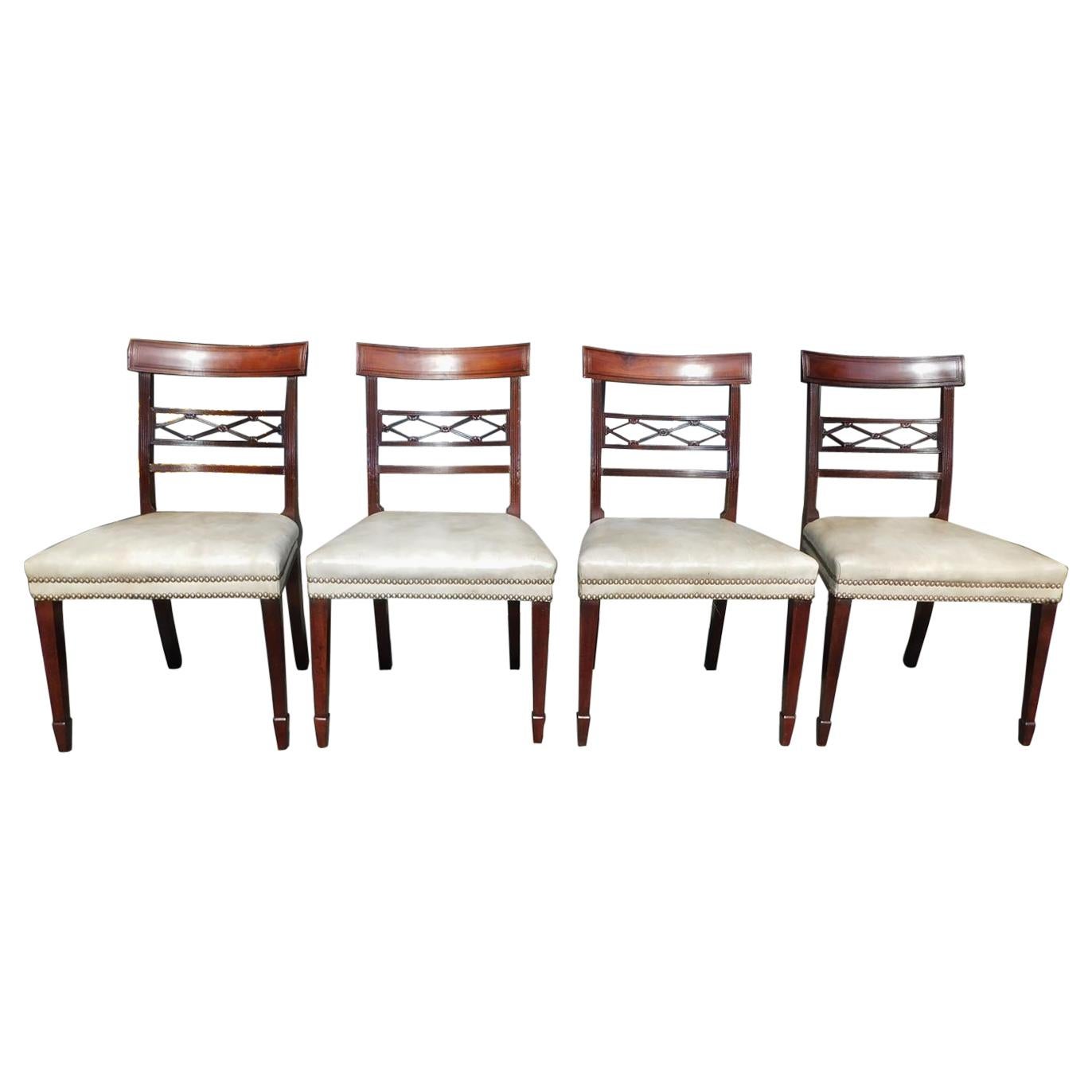 Set of four English Regency mahogany upholstered and brass tacked dining room chairs with floral reeded cross hatching and terminating on tapered squared legs with spade feet. Set consist of four sides. Early 19th century.
