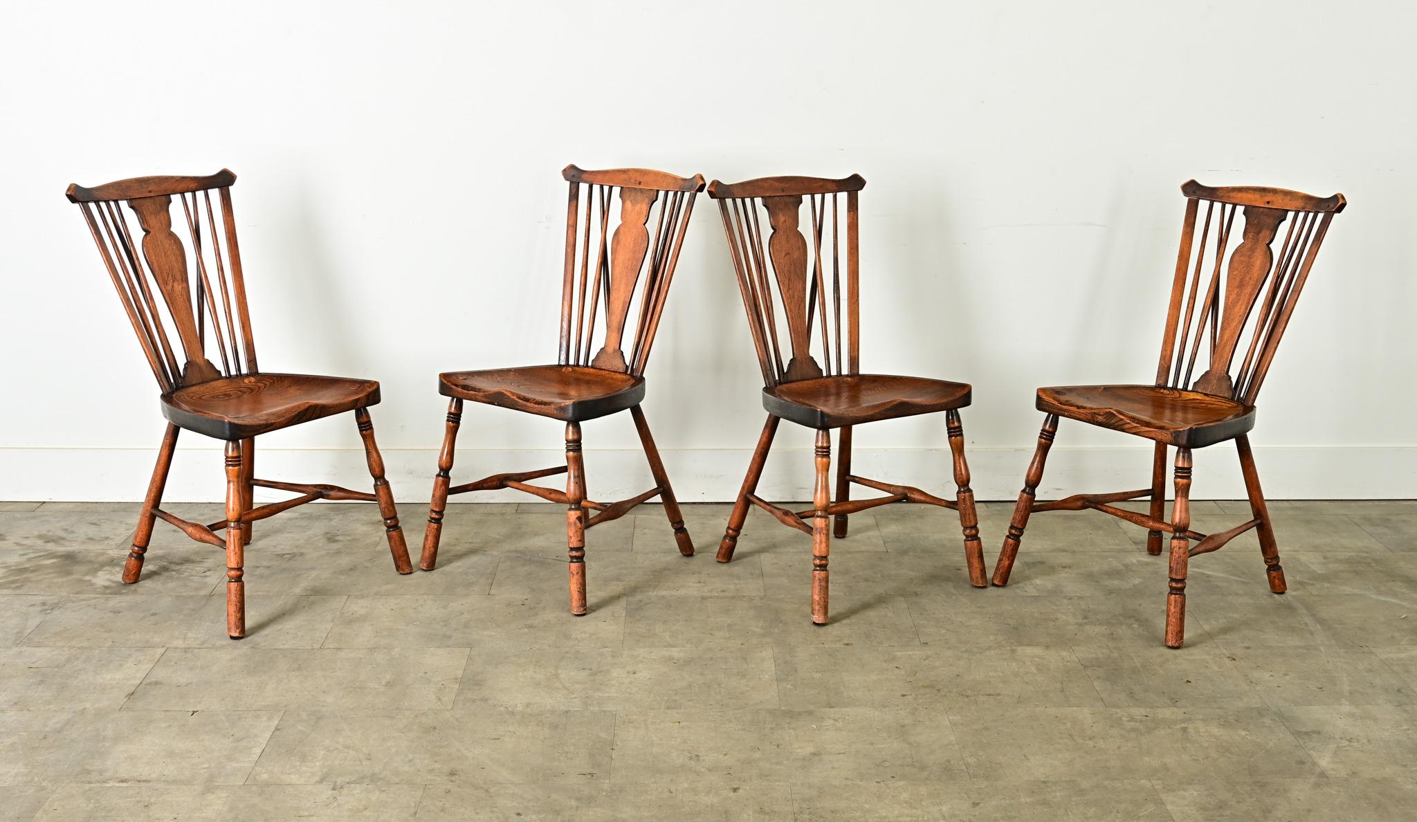 Un set di quattro sedie Windsor inglesi del 1890 circa. Realizzato in quercia, con le vele a forma di arco di bue nella parte superiore che si collegano a stecche sagomate e a sottili fusi per lo schienale. Altri due fusi a V sostengono il corrimano