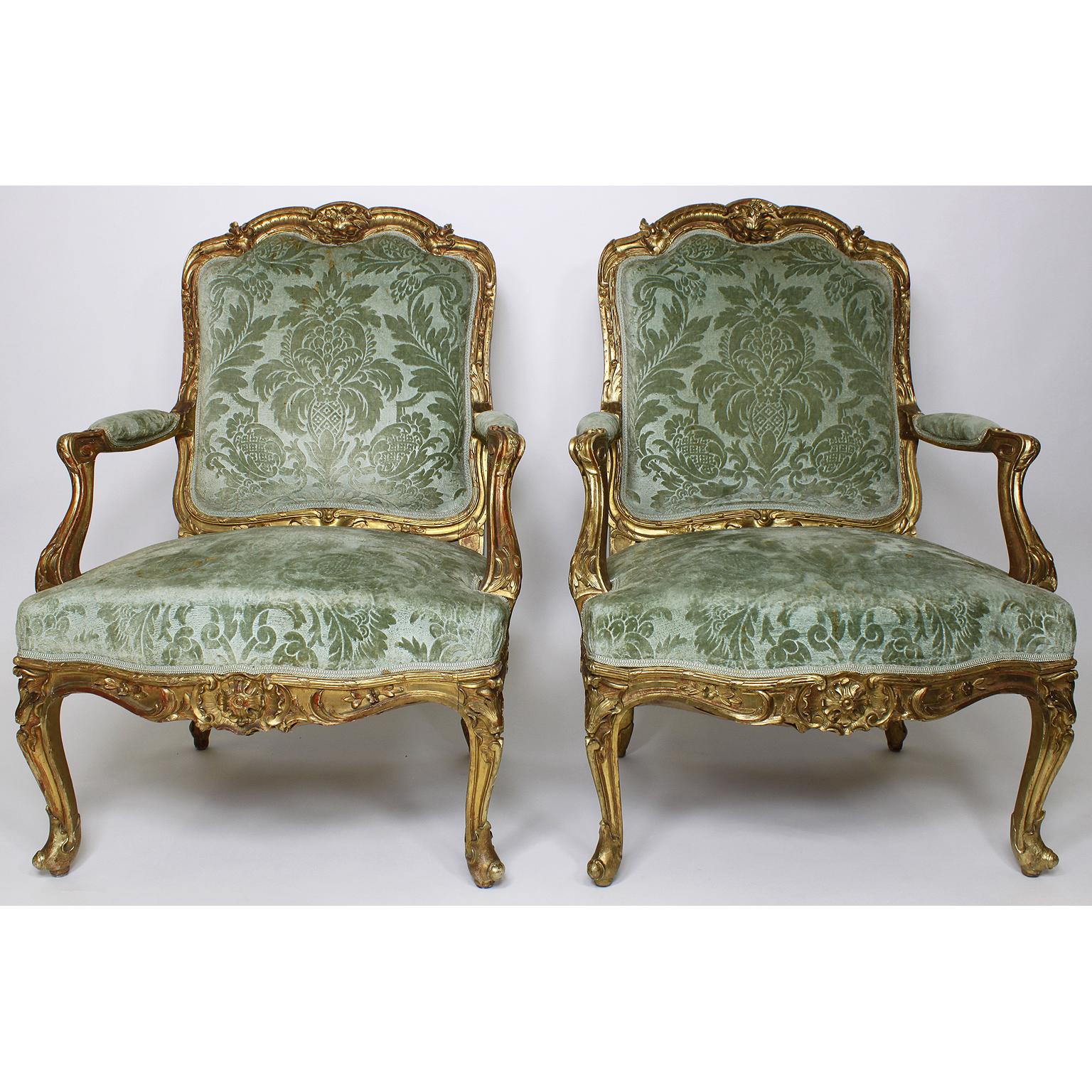 A fine set of four French 19th century Louis XV Rococo style giltwood carved Fauteuil à la Reine armchairs, the arched upholstered paneled backs with foliate scroll cresting and similar borders, having padded arm supports above slip-in seat, raised