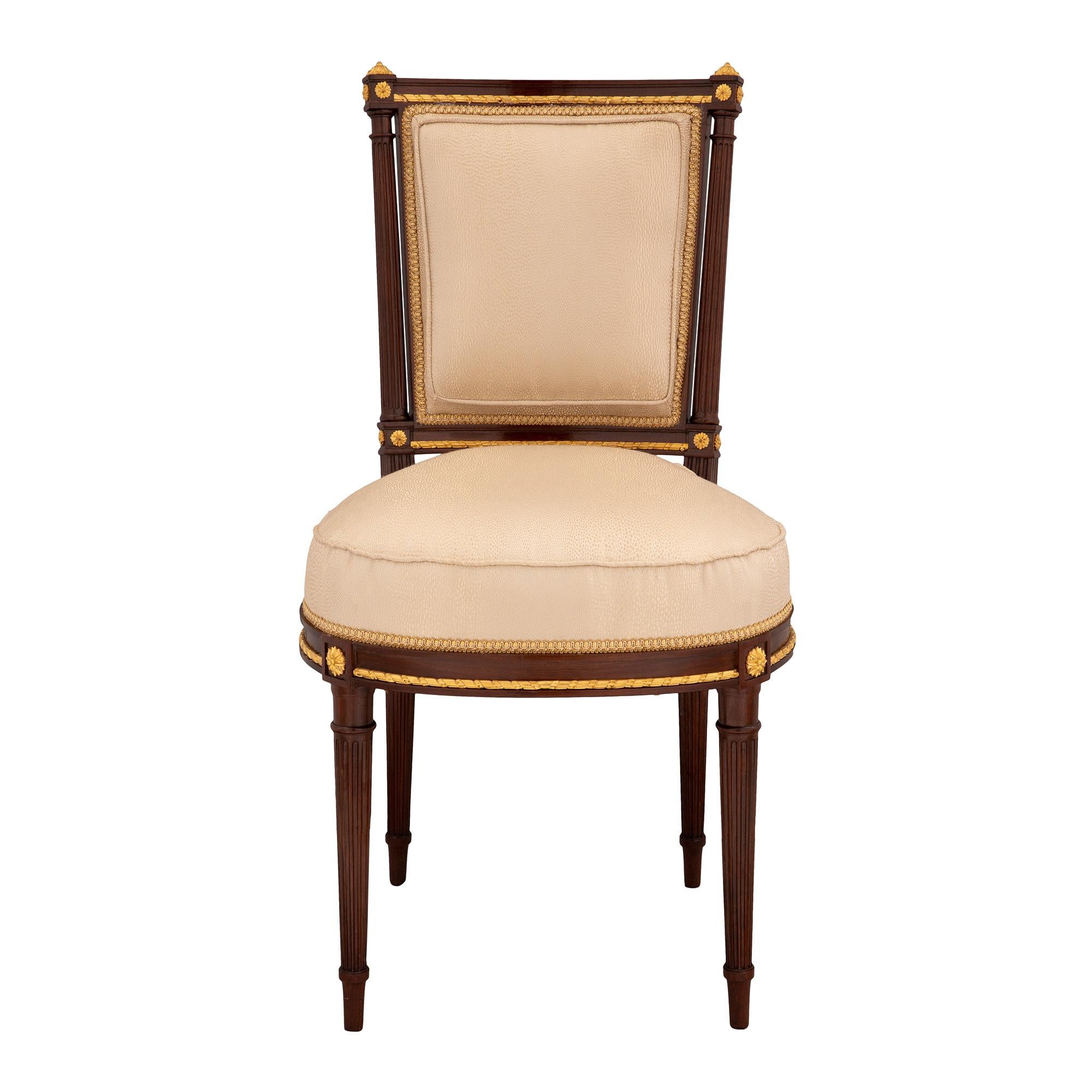 An extremely elegant set of four French 19th century Louis XVI st. mahogany and giltwood side chairs. Each chair is raised by slender circular tapered fluted legs with a finely carved and most decorative giltwood rosette above each leg. A richly