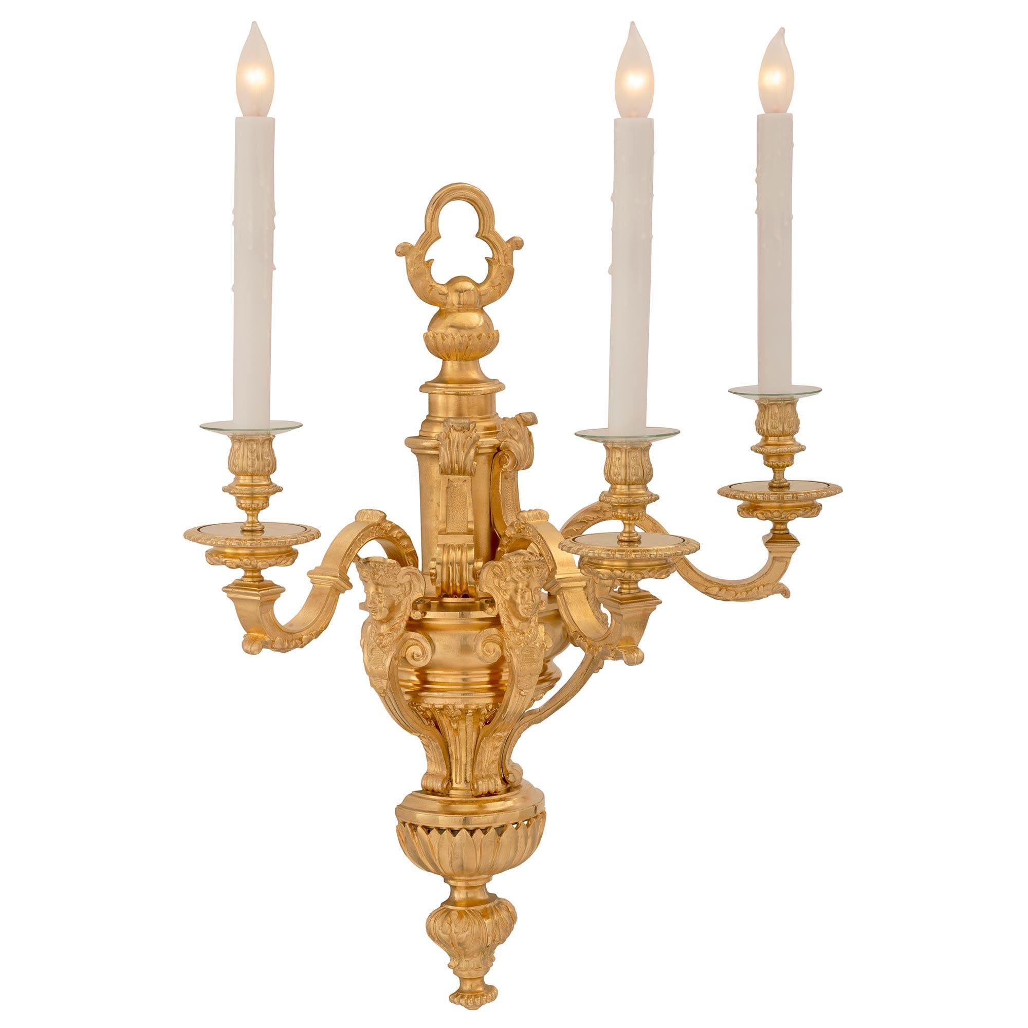 An impressive and high quality complete set of four French 19th century Louis XVI st. ormolu sconces. Each large scale three arm sconce is centered by a lovely foliate bottom finial with an elegant urn shape decorated with fine palmettes. Three