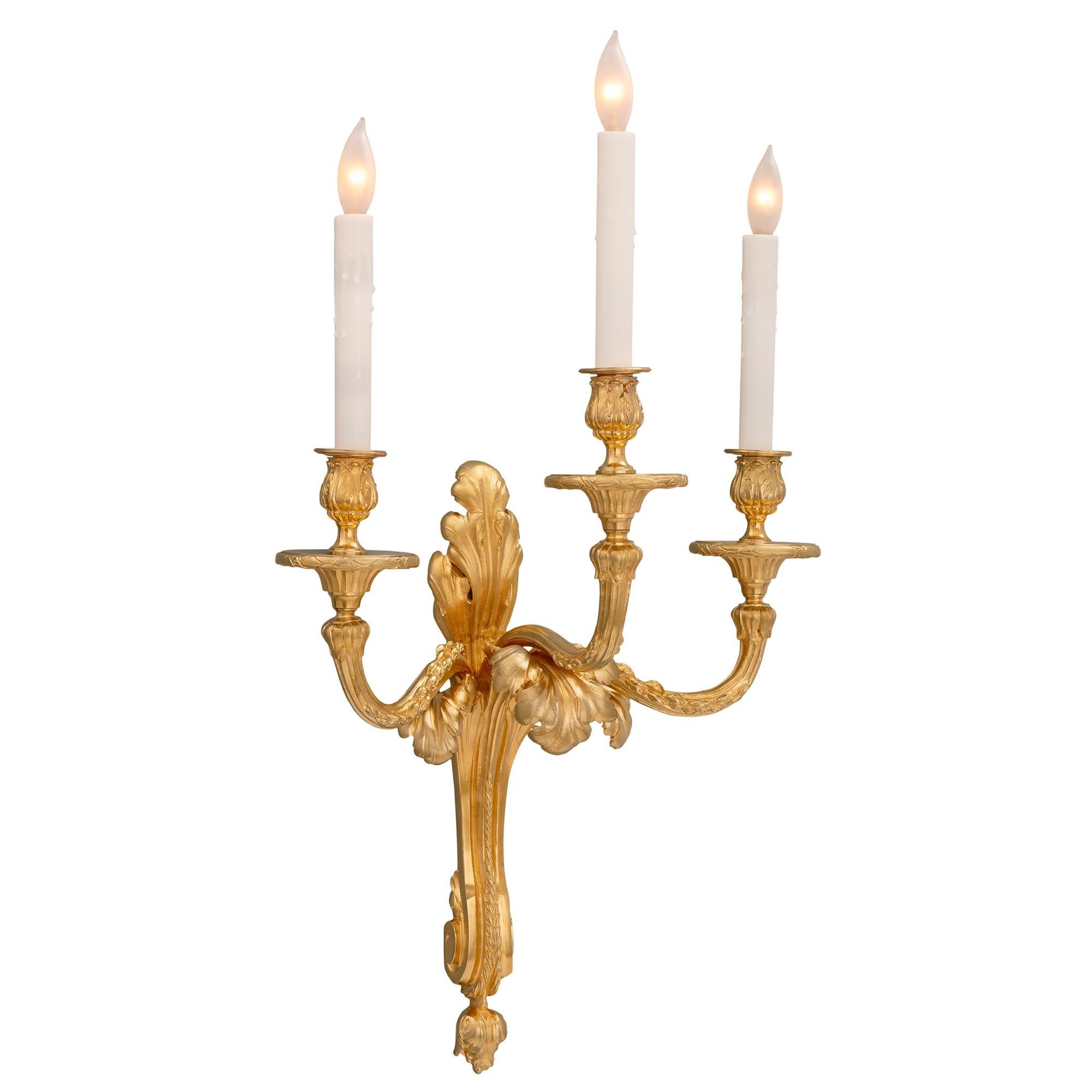 A most elegant and complete set of four French 19th century Louis XVI st. ormolu sconces. Each three arm sconce is centered by a lovely bottom foliate finial below the beautiful scrolled central support with a large richly chased acanthus leaf at