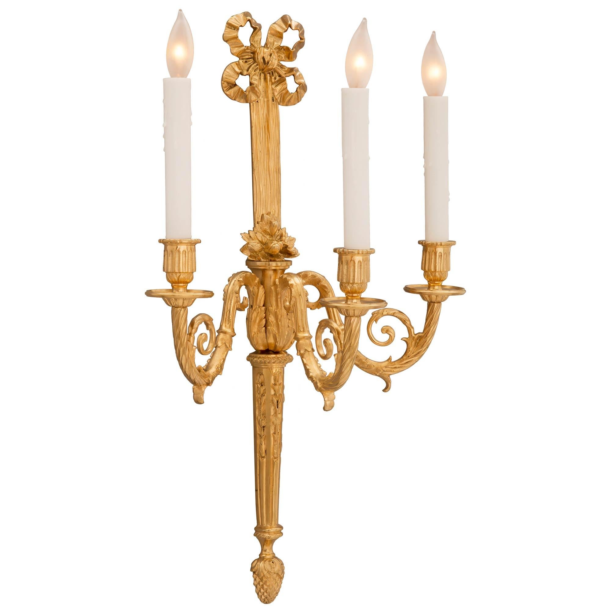 A beautiful and complete set of four French 19th century Louis XVI st. ormolu sconces. Each elegant three arm sconce is centered by a richly chased bottom acorn finial below the tapered fluted central fut decorated with fine foliate chandelles. Each