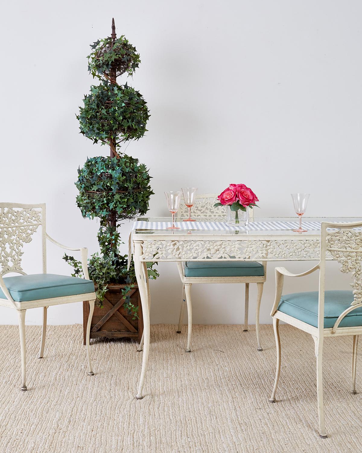Midcentury set of four French floral motif patio, garden, or dining chairs constructed from cast aluminum. The square backs feature a flower cascade splat with gracefully curved armrests. Each chair has a vinyl French blue seat cushion and is
