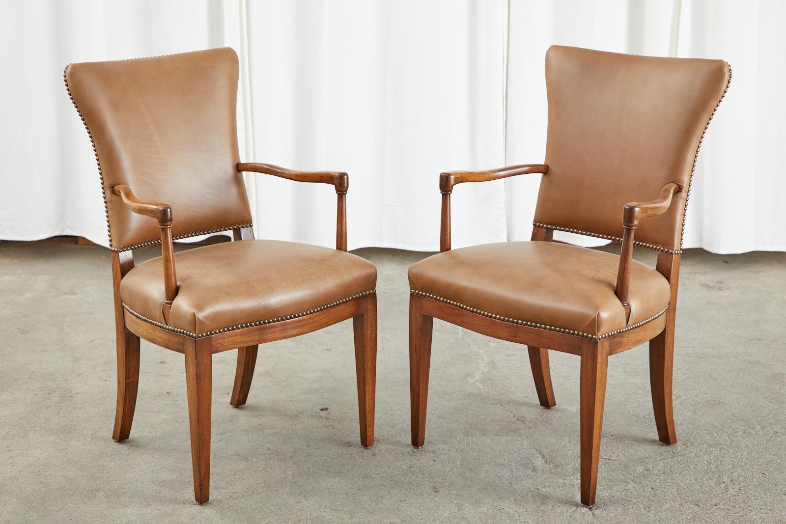 Extraordinary set of four French art deco chairs crafted from radiant mahogany after Jules Leleu. The chairs feature a large flared back with a contoured rest that is upholstered with an aged leather. The back has gracefully curved arms that conjoin