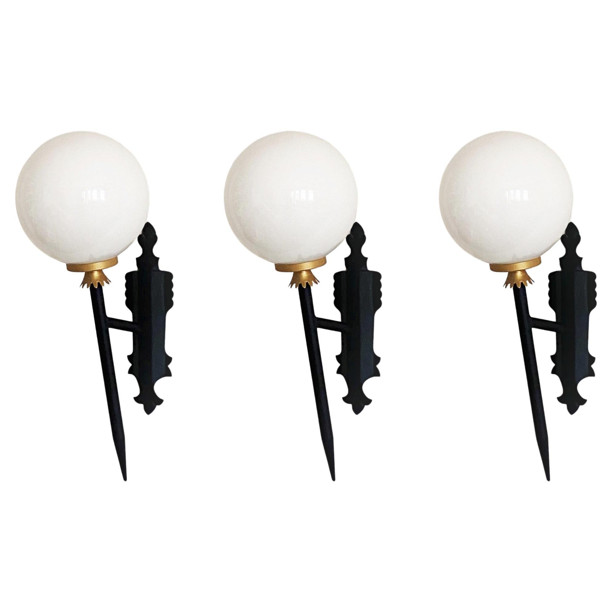 A very elegant set of four Arte Deco black painted wrought iron parcel brass torchiere wall lights with opaline glass ball globes, for indoor and outdoor use, France, 1950s. 
The wall sconces are in very good condition, beautiful patina, rewired