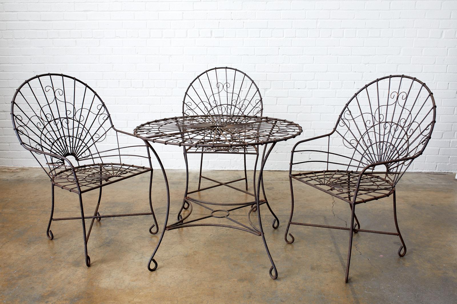 Distinctive set of four French Art Nouveau iron and wire patio garden chairs. The chairs feature a fan back or peacock style back design with wire work decorating the frames. Supported by legs ending with whimsical looped feet. Beautifully aged