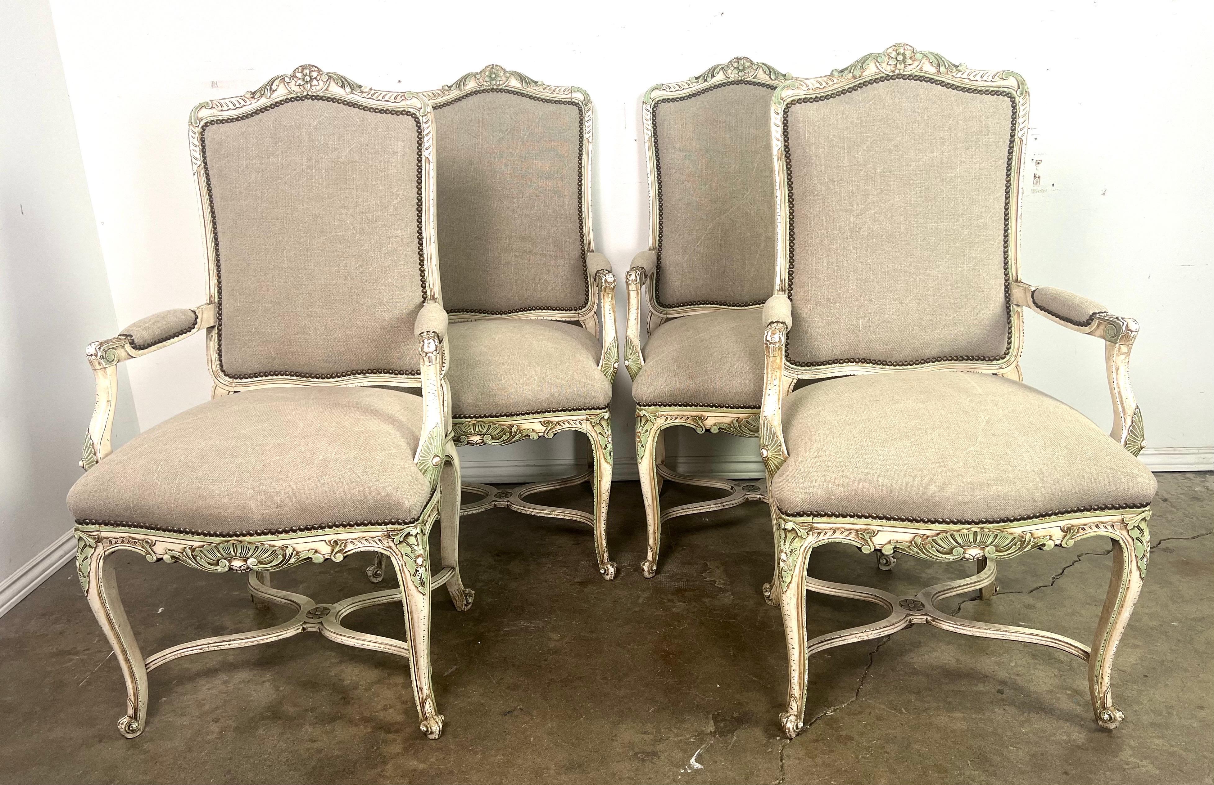 Ensemble de quatre fauteuils peints de style Louis XV.  Les fauteuils sont revêtus d'un lin belge lavé et d'une garniture à tête de clou.  Le cadre en bois est orné de motifs floraux et de volutes.  Ces détails sont accentués par la finition de
