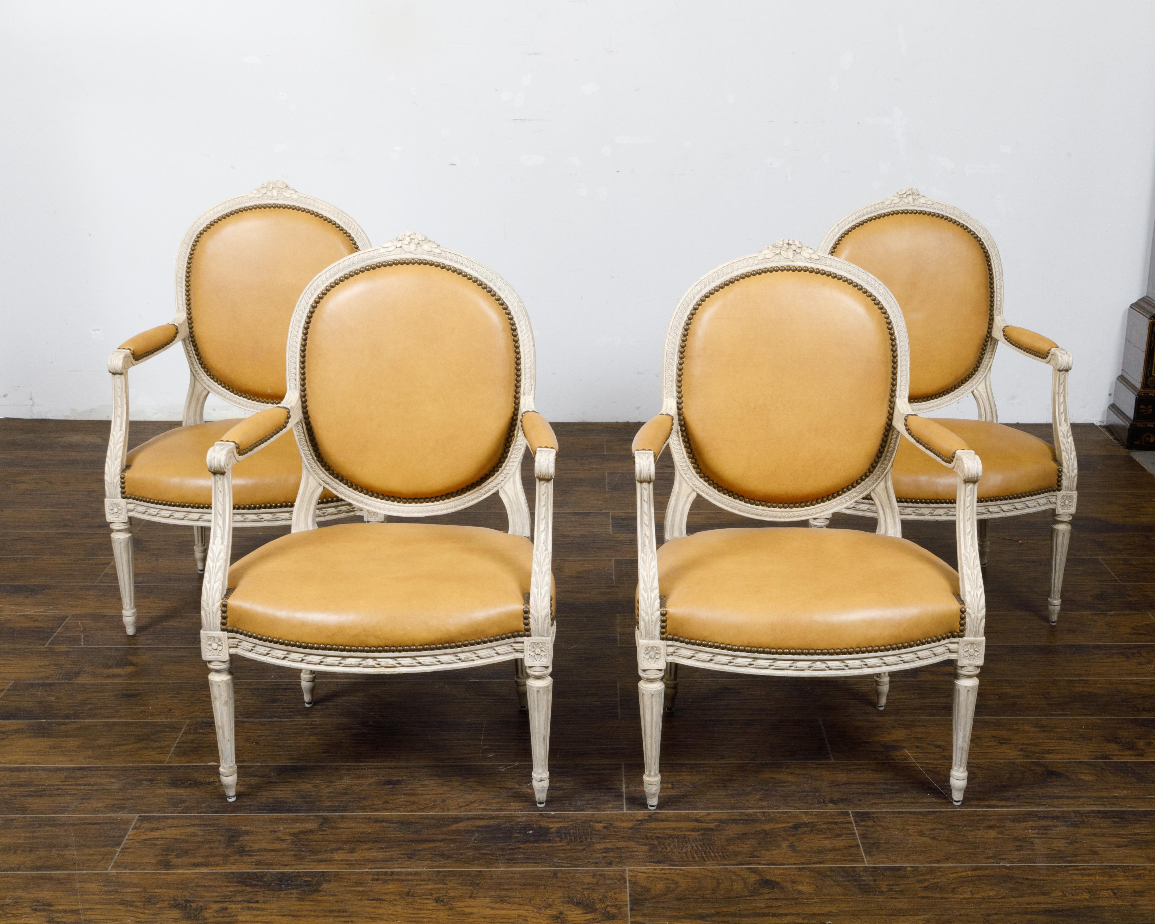 A set of four French Louis XVI style off-white painted oval back armchairs from circa 1900 with carved décor. This set of four French Louis XVI style armchairs, dating back to circa 1900, features an elegant off-white painted finish with traces of