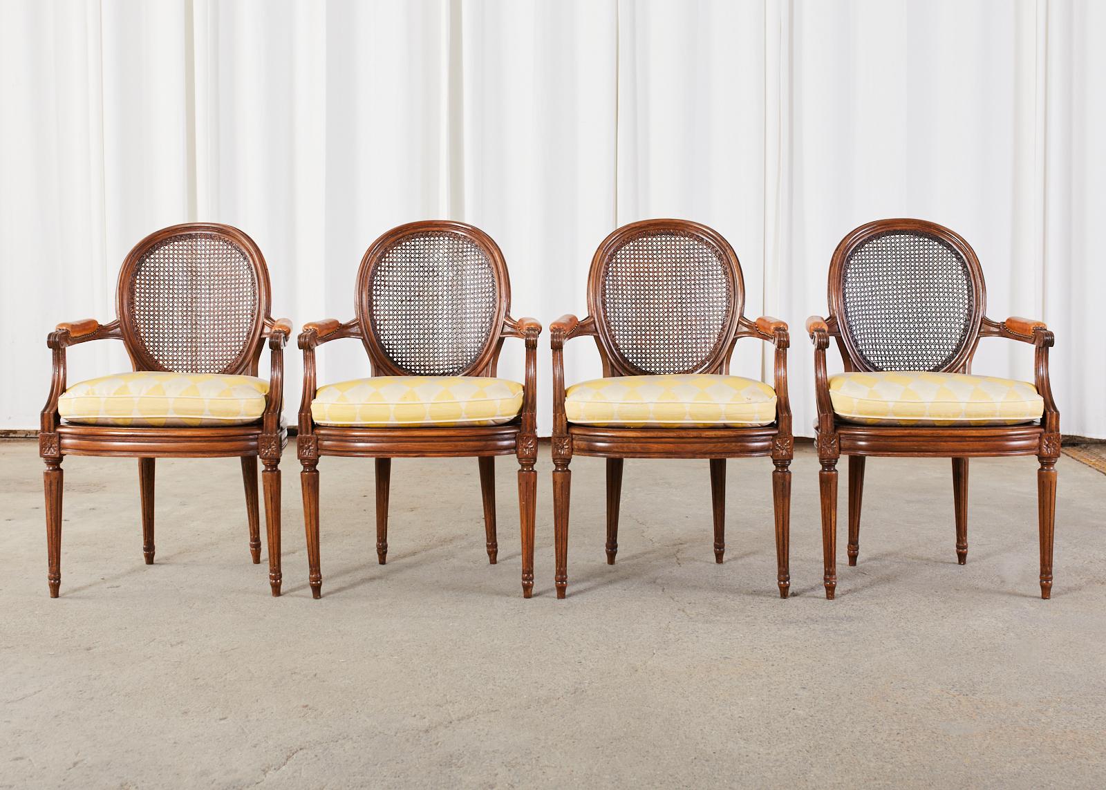 Handsome set of four French mahogany dining armchairs featuring round cane backs and cane seats. Hand-crafted in the grand Louis XVI taste having molded arms and bowed seat decorated with rosettes. The leather padded arms measure 27 inches high and