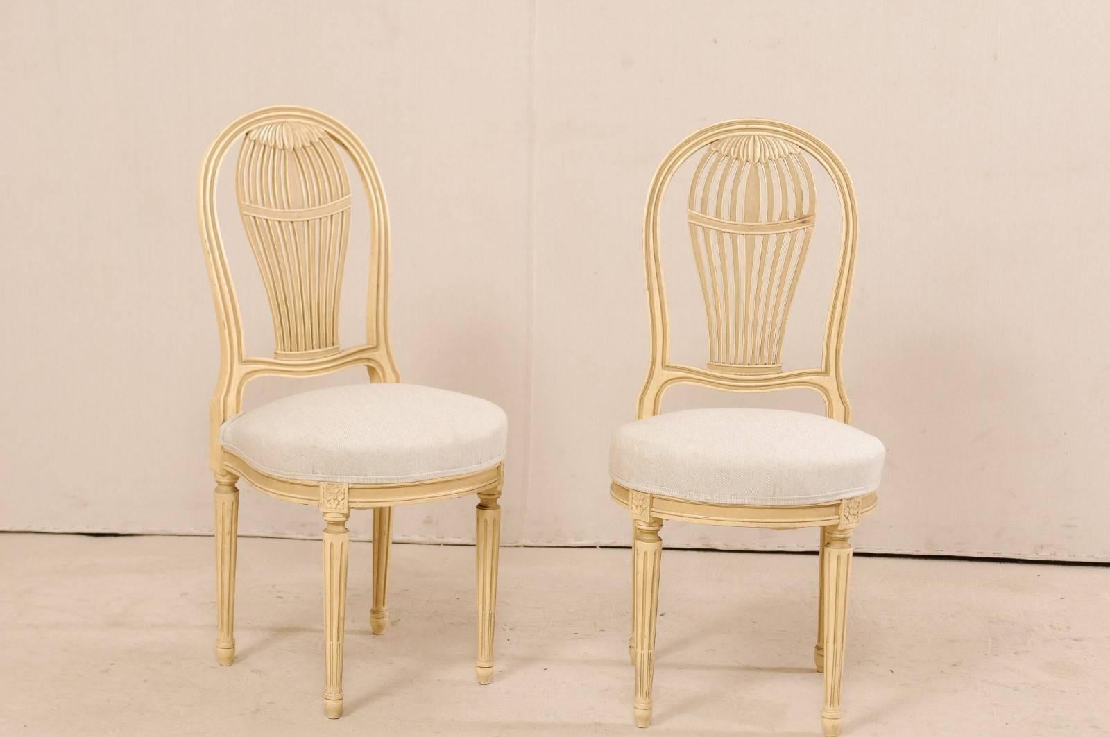 A set of four French Louis XVI style painted wood and upholstered side chairs from the mid-20th century. This set of vintage French chairs feature beautiful balloon backs, reminiscent of 18th century hot air balloons, rounded front skirts with