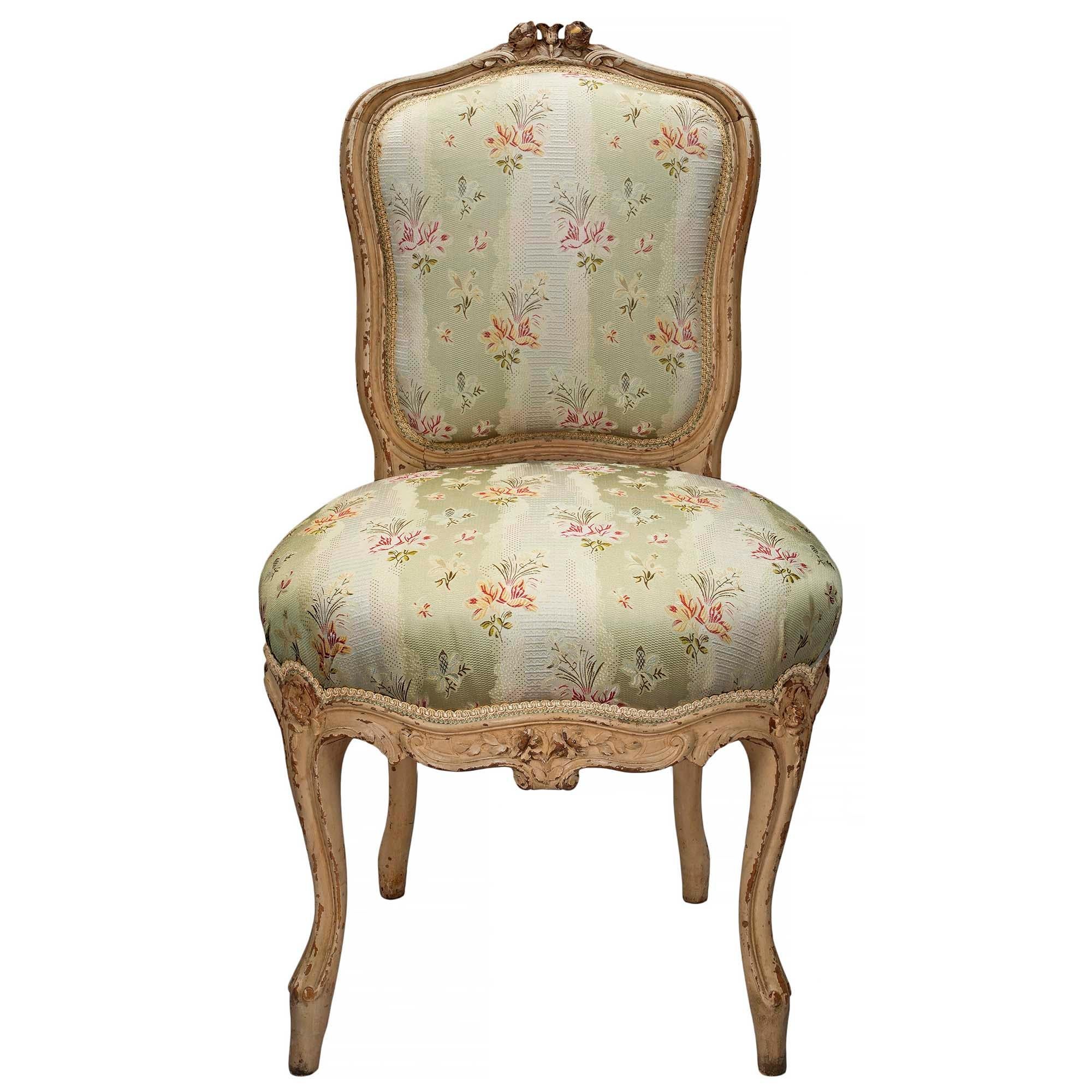 An exquisite and elegant set of four French mid 19th century Louis XV st. richly carved, patinated off-white chairs. The set is raised by 's' scrolled cabriole legs below a scalloped design frieze with carvings of flowers and foliage. The violin