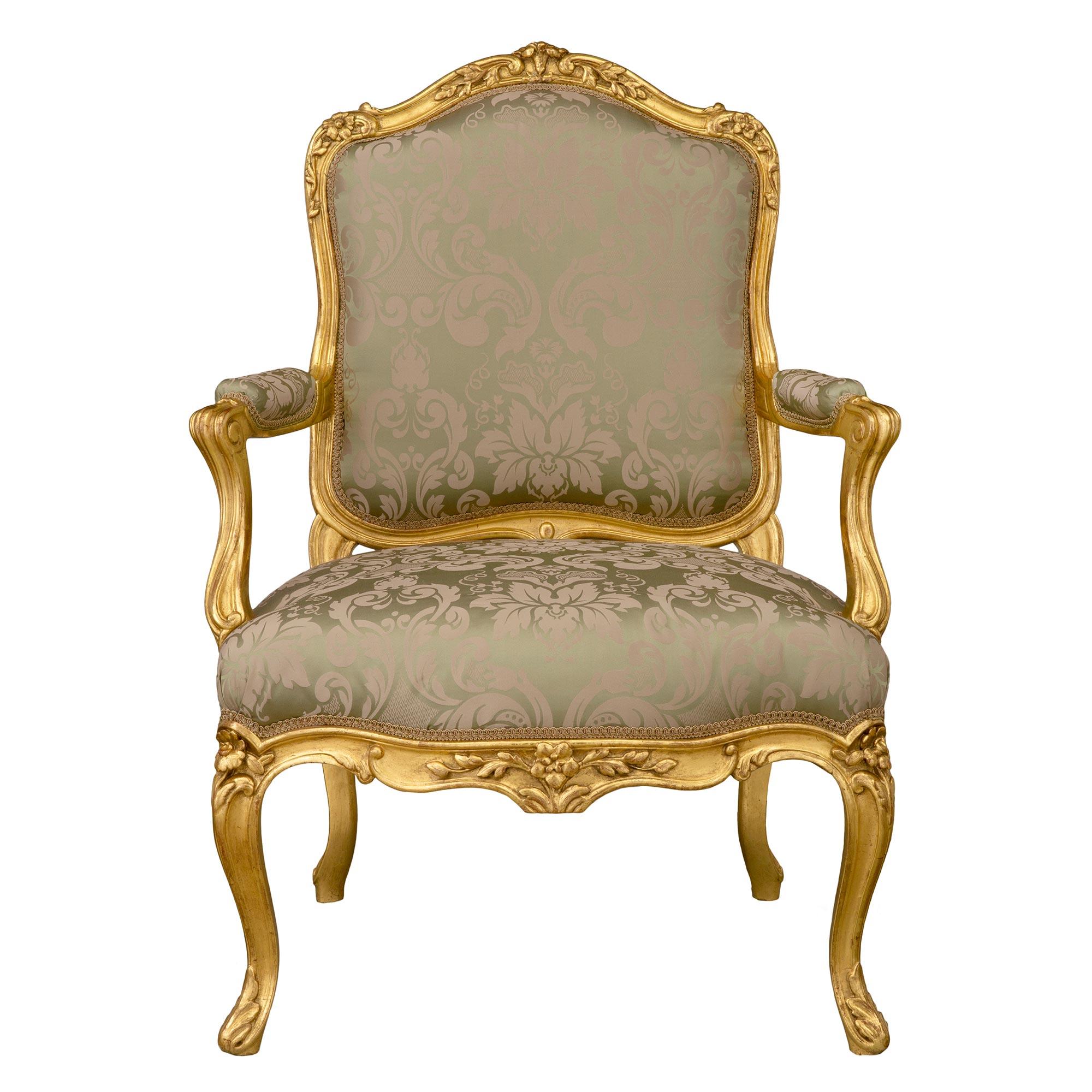 An elegant set of four French mid 19th century Louis XV st. giltwood armchairs. Each armchair is raised by beautiful cabriole legs with richly carved acanthus leaves and lovely finely detailed flowers which extend along the scallop shaped apron.