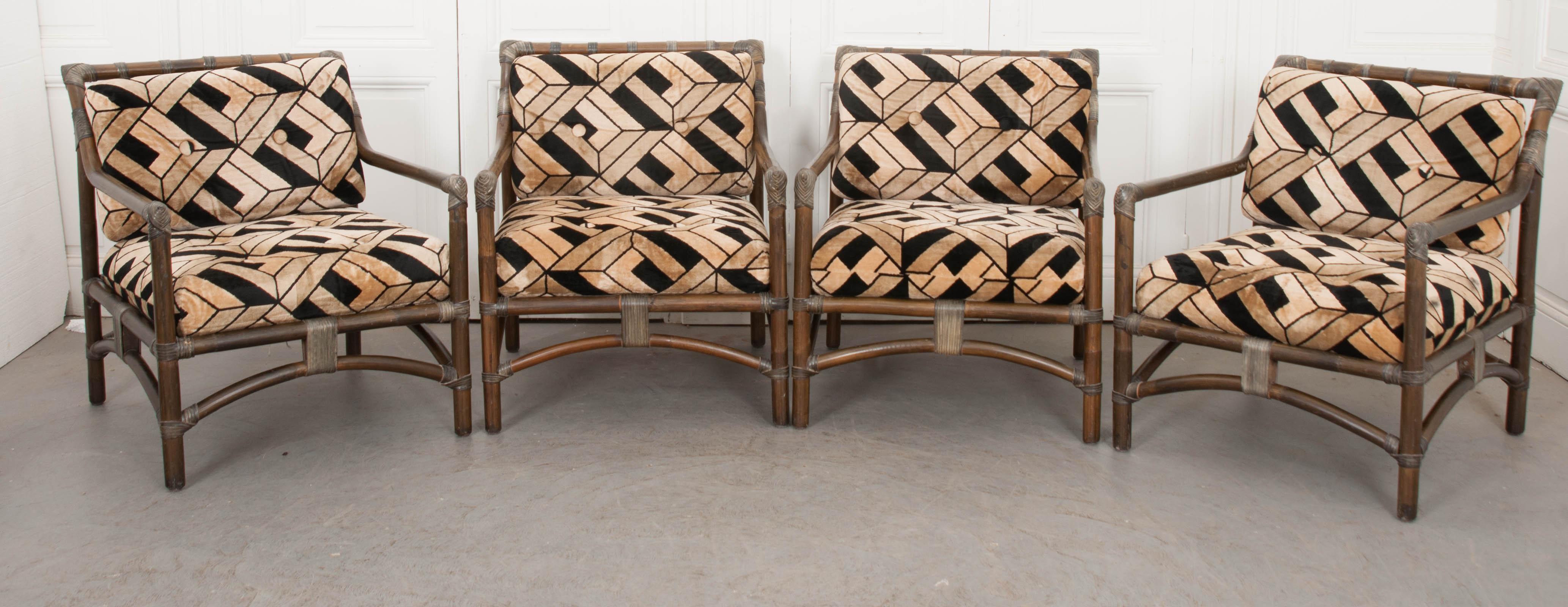 This fantastic set of four Mid-Century Modern rattan armchairs, circa 1970s, are from France. These chairs have leather strap accents and are newly upholstered in a fabulous black and creamy-gold geometric velvet upholstery reminiscent of the era.