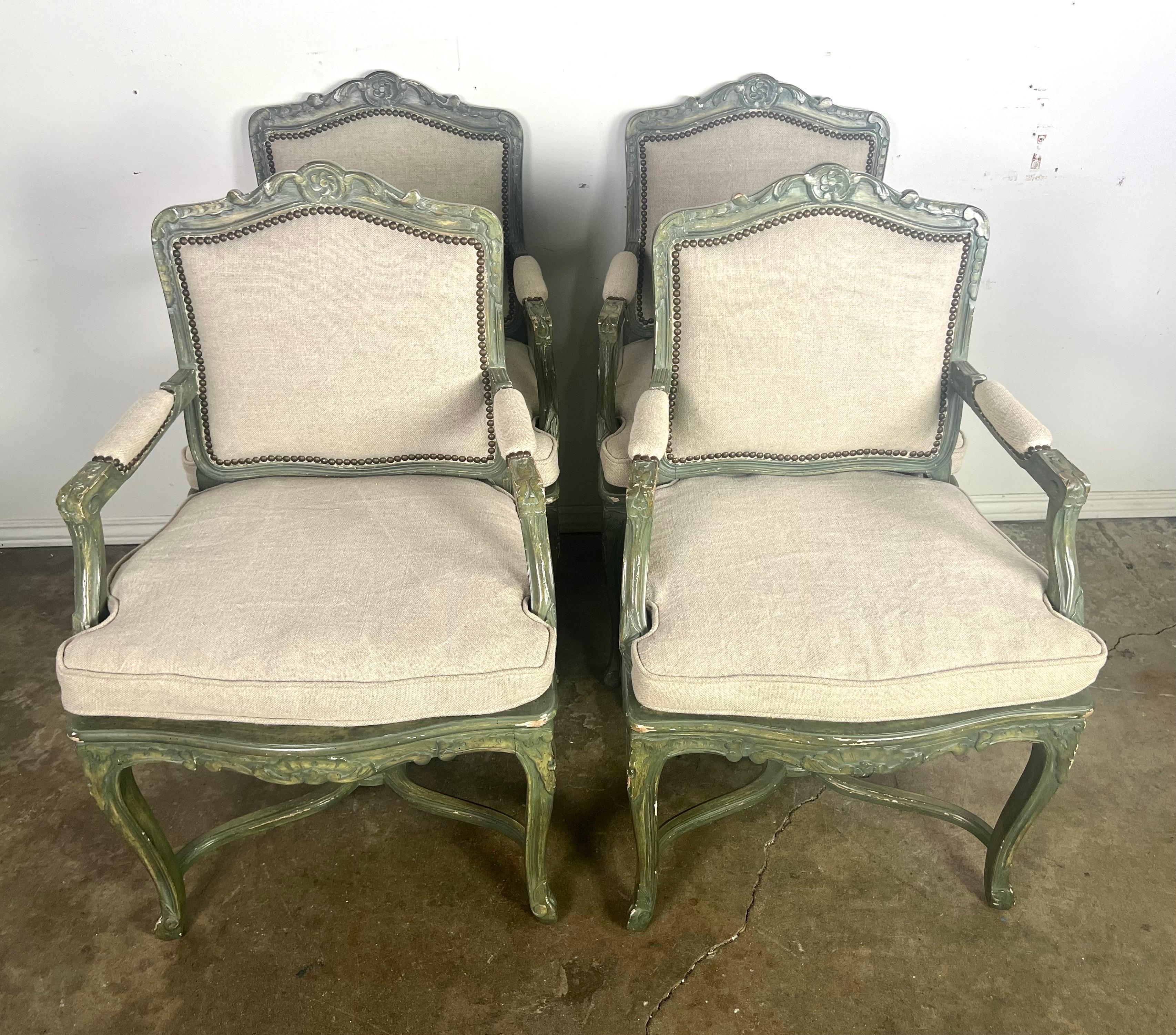 This set of chairs are beautifully crafted  in a Louis XV style, featuring a distinctive painted frame in a soft green hue with subtle gilt accents.  The chairs are adorned with elegant, open arms and stand on gracefully curved cabriole legs.  The