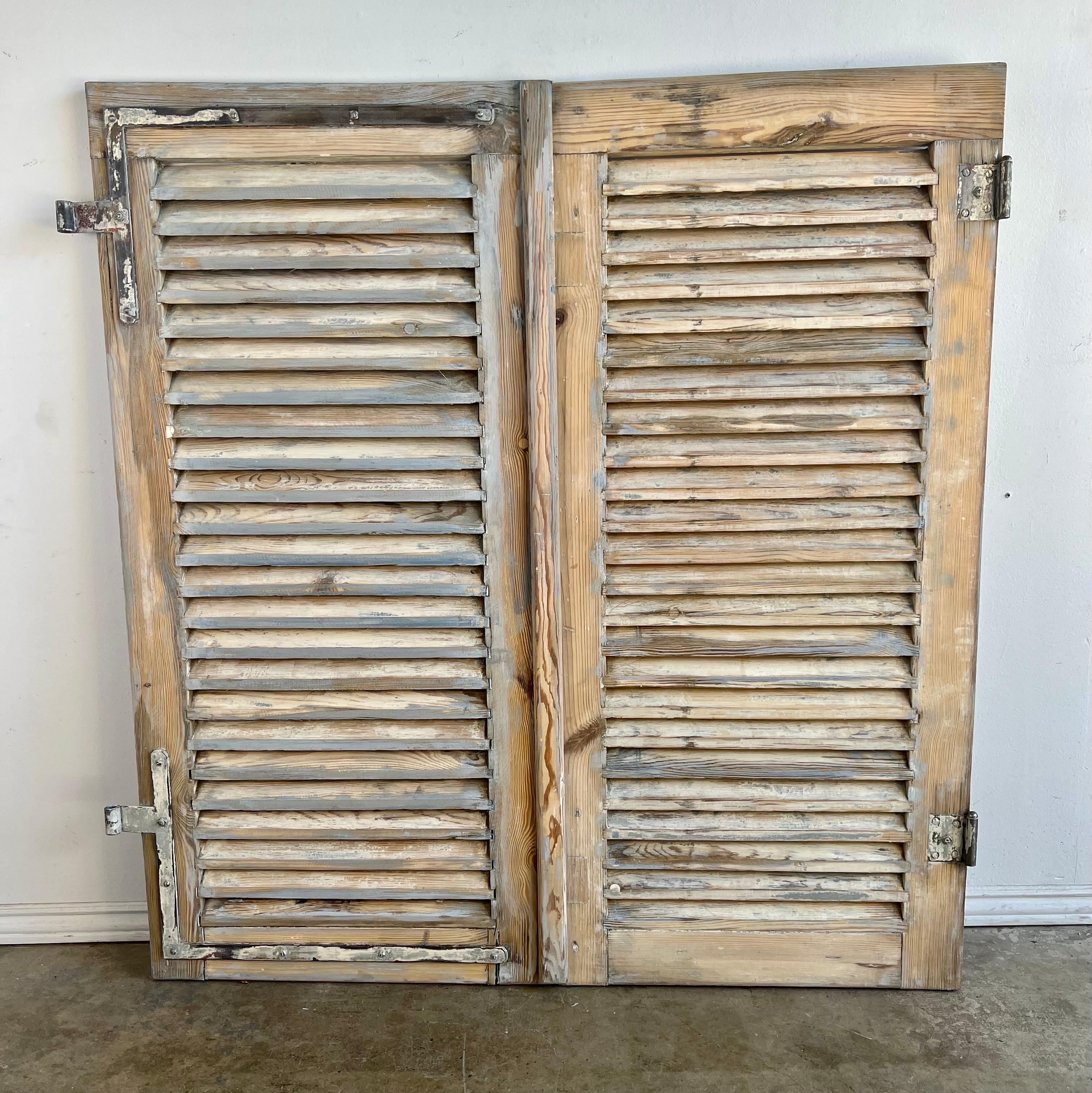 French provincial painted pair of shutters with original hardware. The worn finish is missing most of the original paint. There are two sets of shutters available. Each individual shutter measures 24