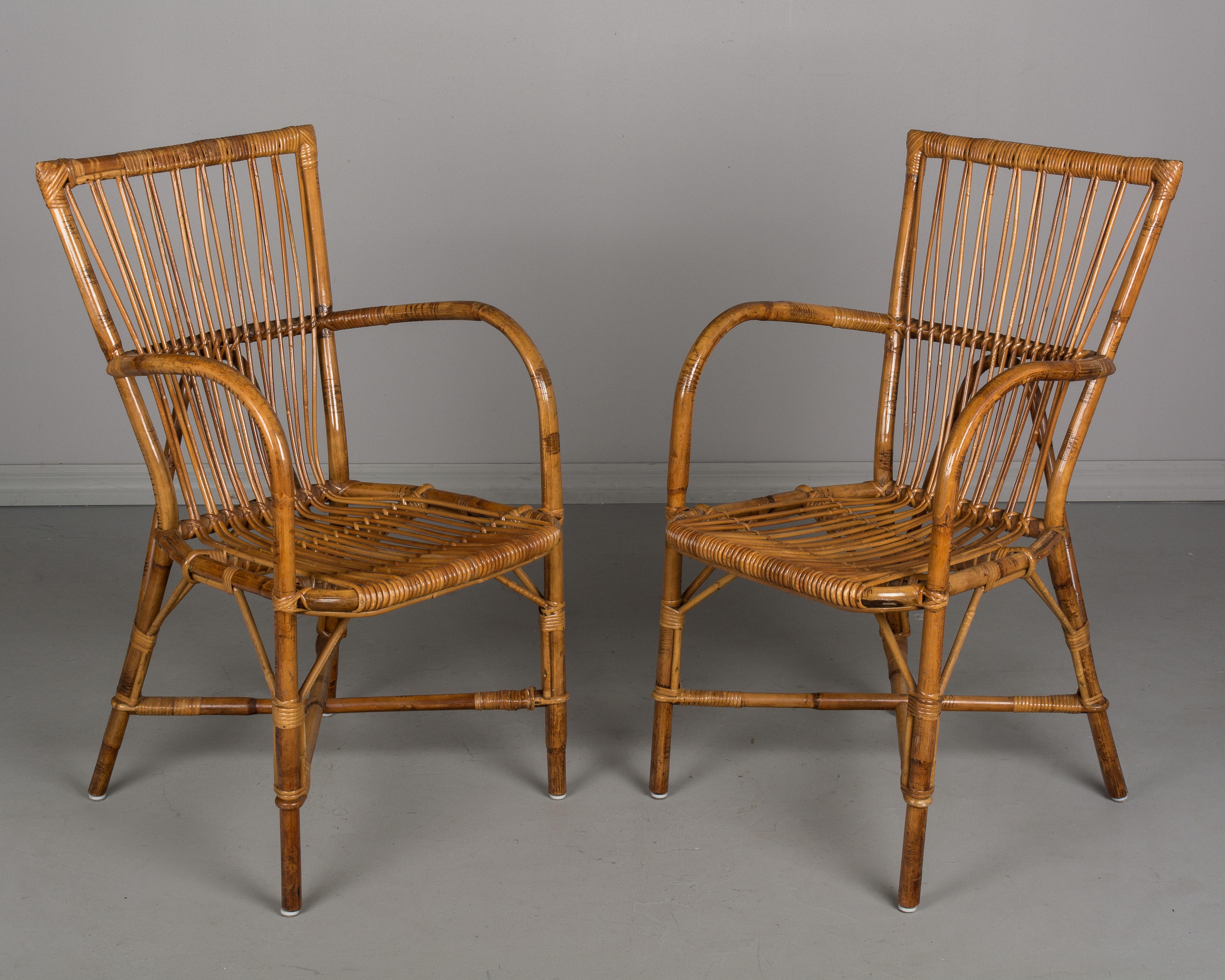 A set of four French midcentury Riviera style rattan dining chairs designed by Audoux-Minet in Golfe Juan. Two arm chairs and two side chairs. Sturdy chairs with comfortable seating.
Measures: Armchairs: 19.5