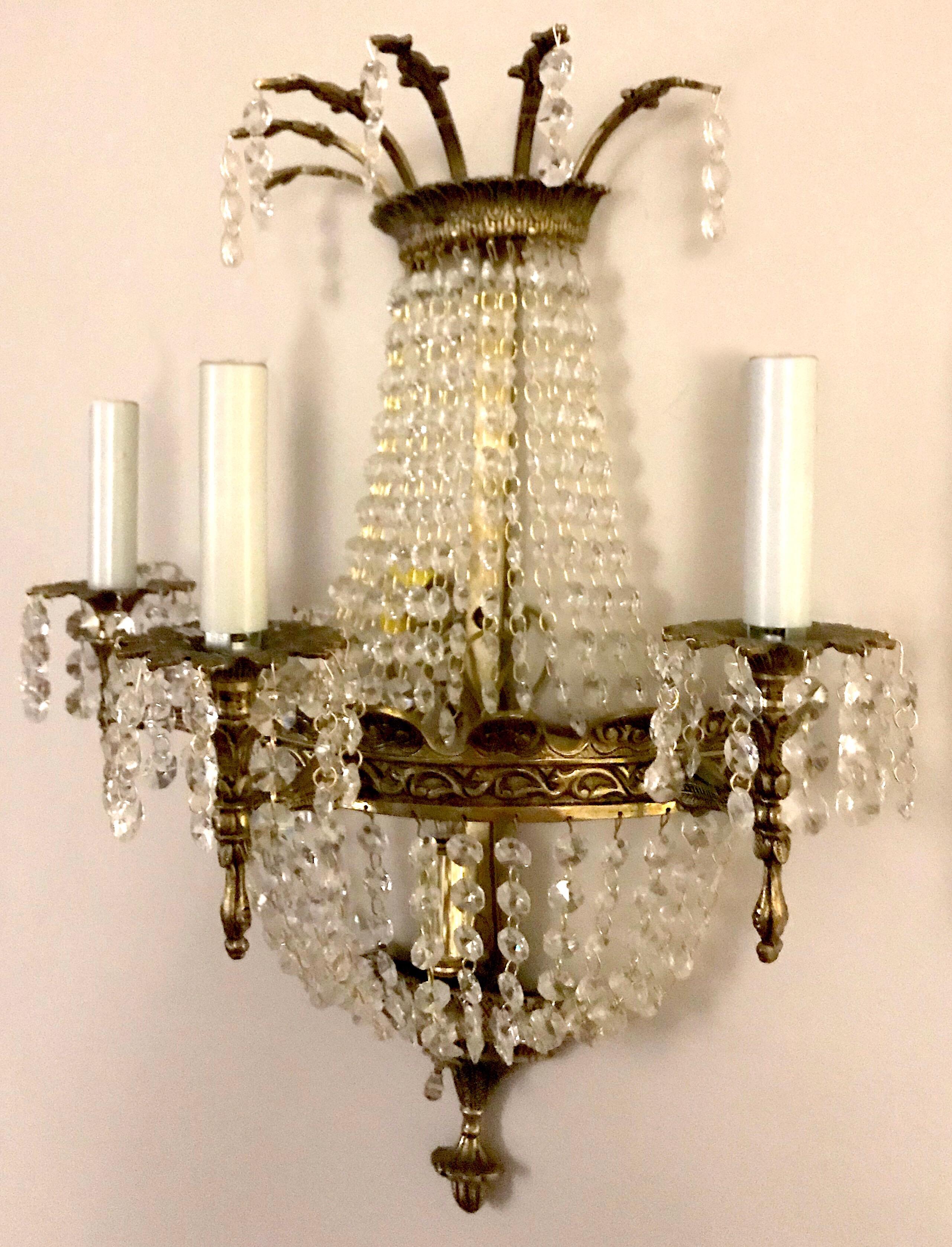 A set of four French style crystal sconces. Each gilt metal sconce has three lights and octagonal prism drops. Sold in pairs.