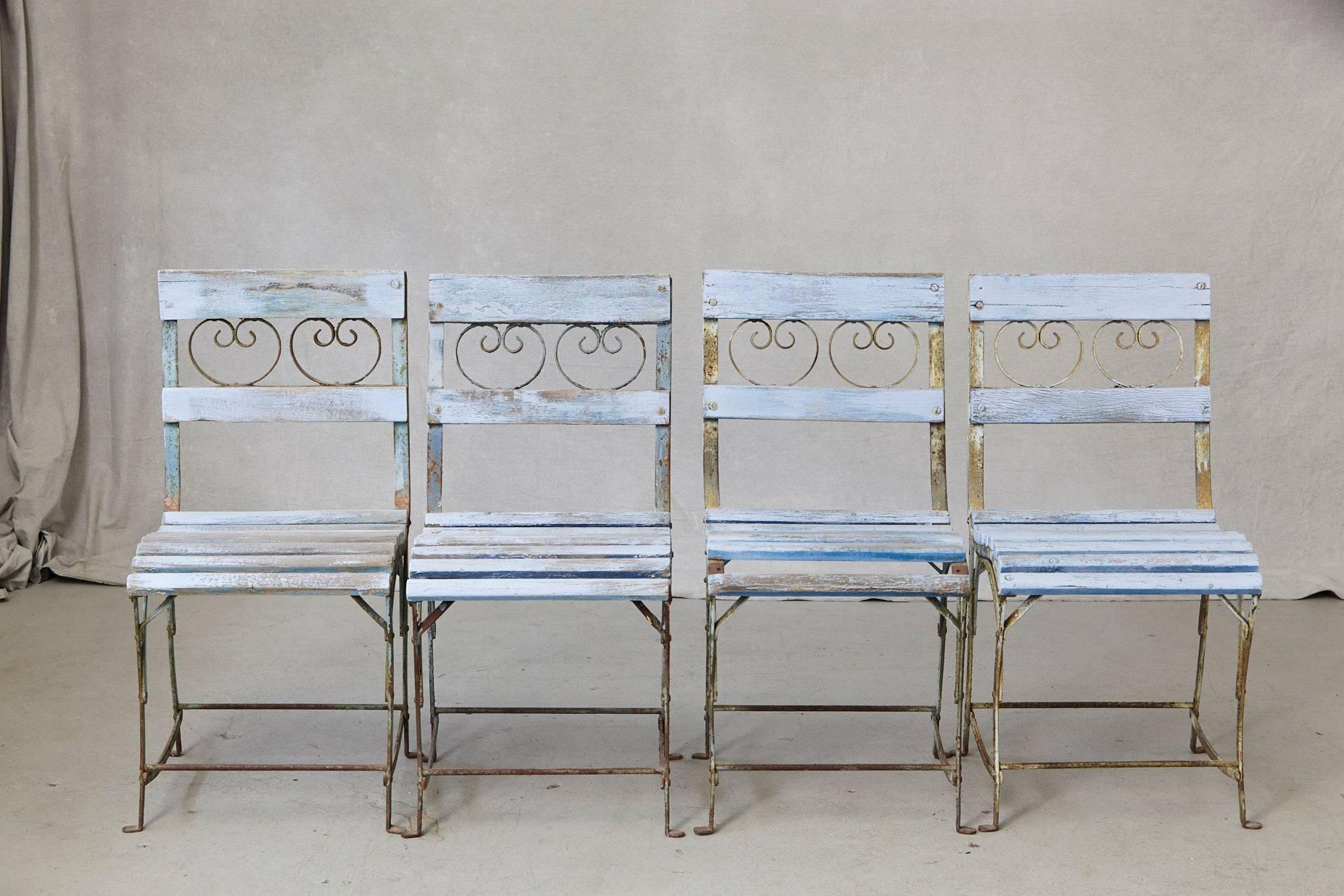 Beautiful set of four French wrought iron garden chairs with blueish wooden slats, circa 1920s.
The chairs have been painted at one point in their life, the blue is faded out, there are paint chips and loss very charming look, beautifully weathered