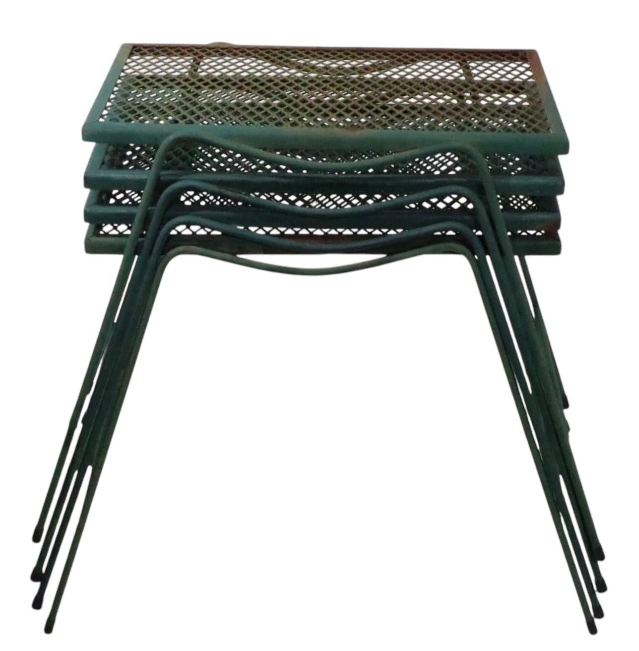 Set of four wrought iron and metal mesh side, or end, tables attributed to the Woodard Furniture Company. The tables feature a lyrical curved skirt profile, with canted legs, and rectangular metal mesh tops. All are structurally  sound and sturdy,