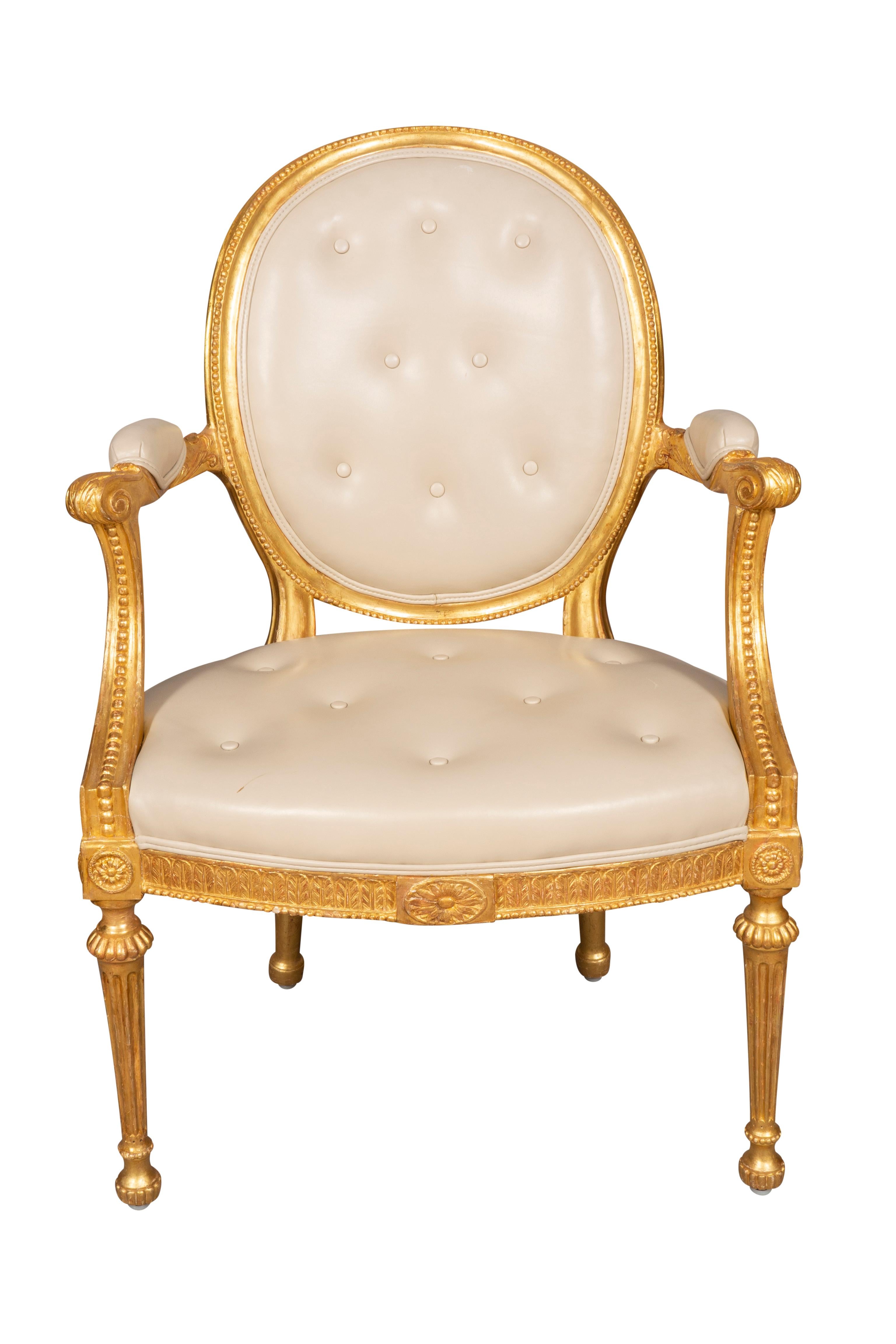 Regilded in burnished gold leaf. Each with oval backs with a carved beaded frame, carved arms with scroll hand hold, leaf carved seat rail with paterae, raised on circular tapered fluted legs. Beautifully upholstered in creme colored leather. From