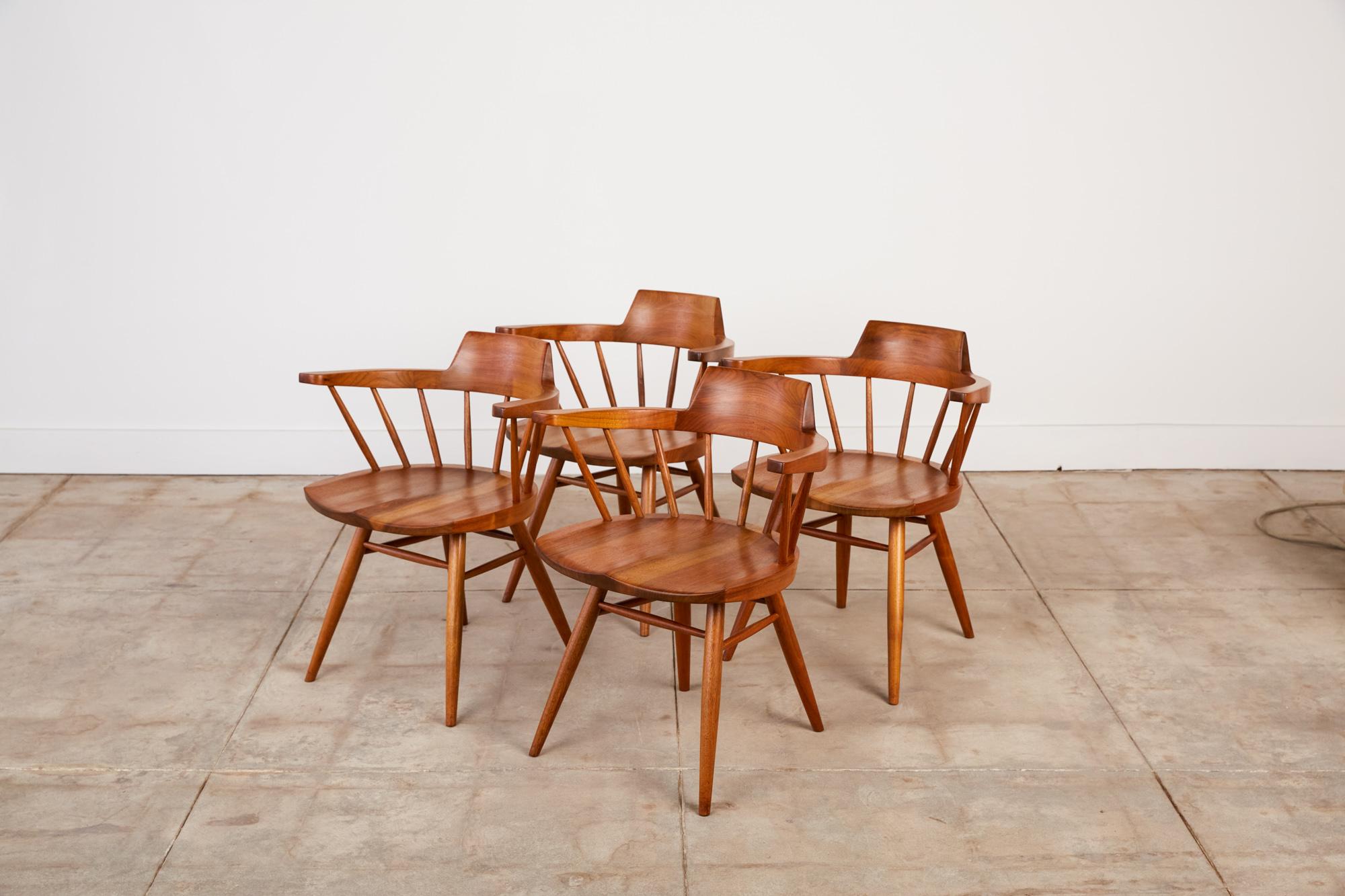 An accomplished set of four captain chairs from American midcentury craftsman George Nakashima. The black walnut chair has a curved, peaked backrest atop carved spindles, inspired by the Windsor chair and Shaker pieces. The seat is hand-sculpted for