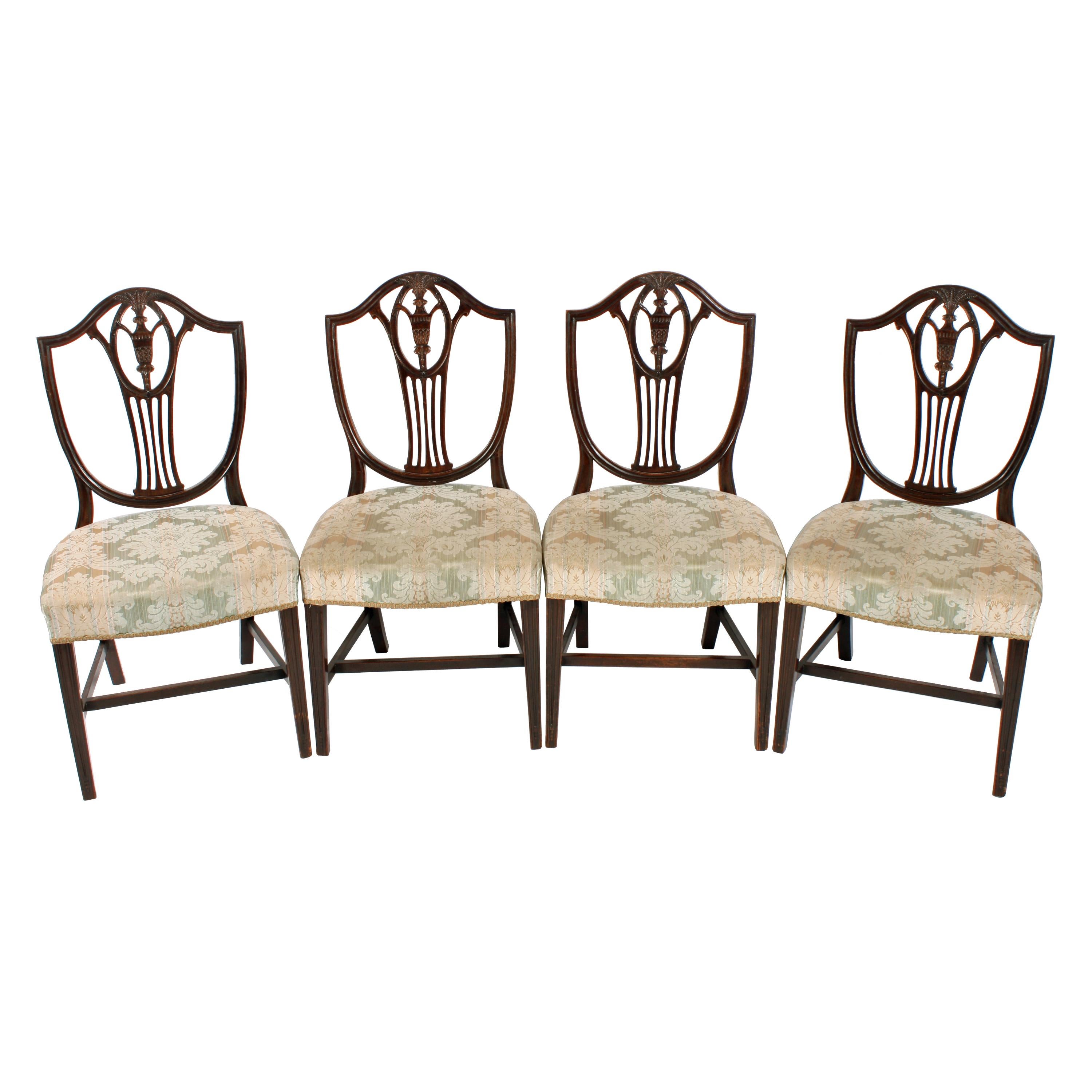 A set of four late 19th century Hepplewhite design mahogany dining room chairs.

The chairs are in a very good Georgian style with shield shaped backs that have a pierced centre splat decorated with a carved urn and wheat sheaths.

The chairs