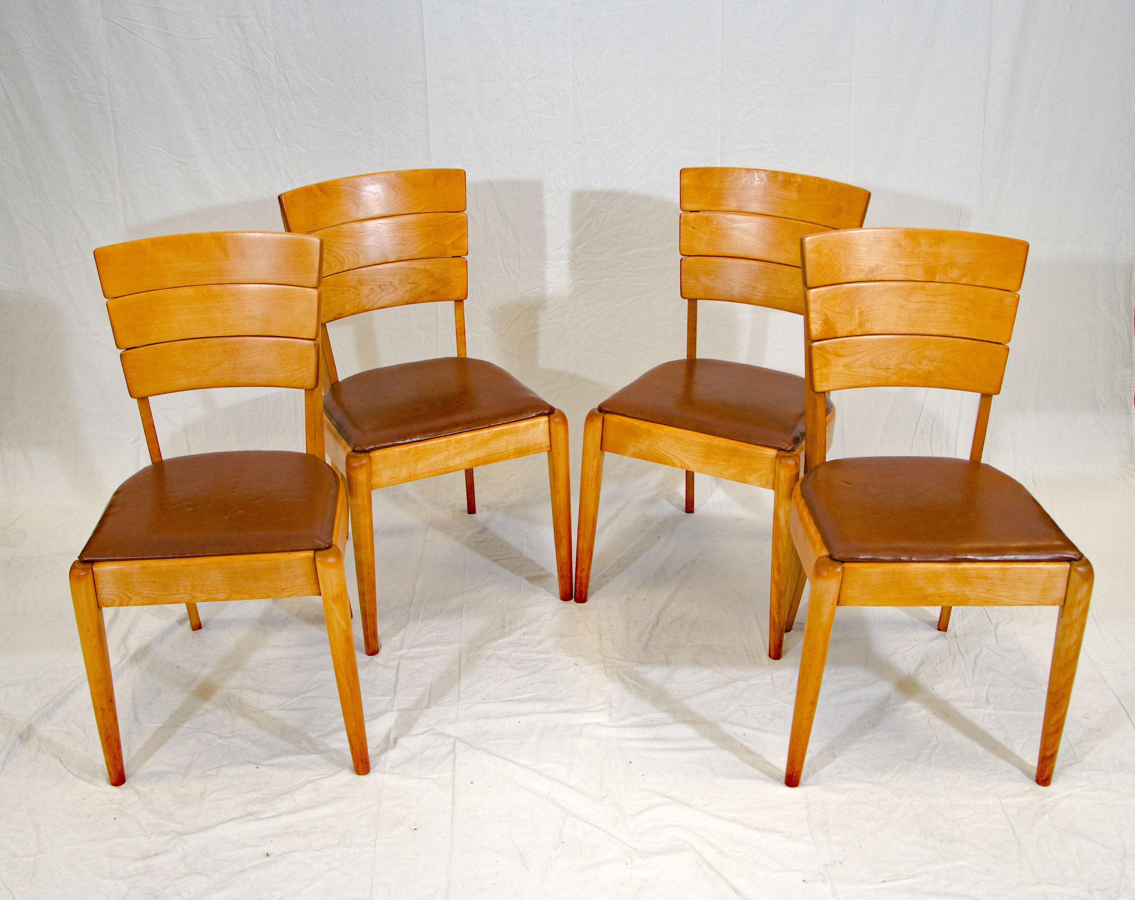 This unusual set of four Heywood Wakefield dining chairs were manufactured from 1937-1942 and are considered to be their early streamlined modern Art Deco period. The back is styled with three graduated wooden sections. The dark brown vinyl seat