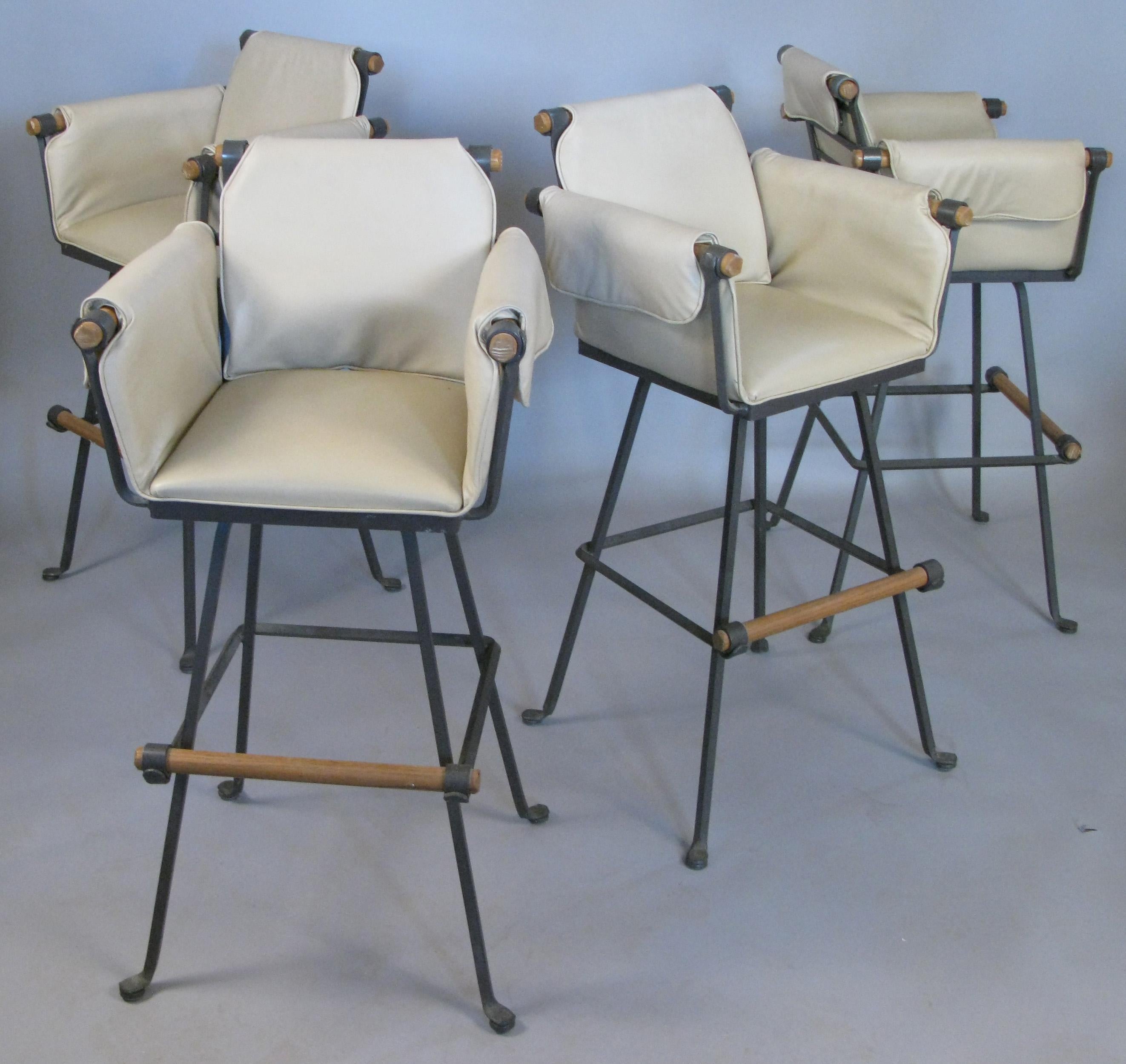 A beautiful set of four vintage 1970s swivel barstools with wrought iron frames and oak arms and footrests. With their original ivory vinyl upholstered seats and arms. Labelled terra furniture. Rare to find in a set this large and in very good
