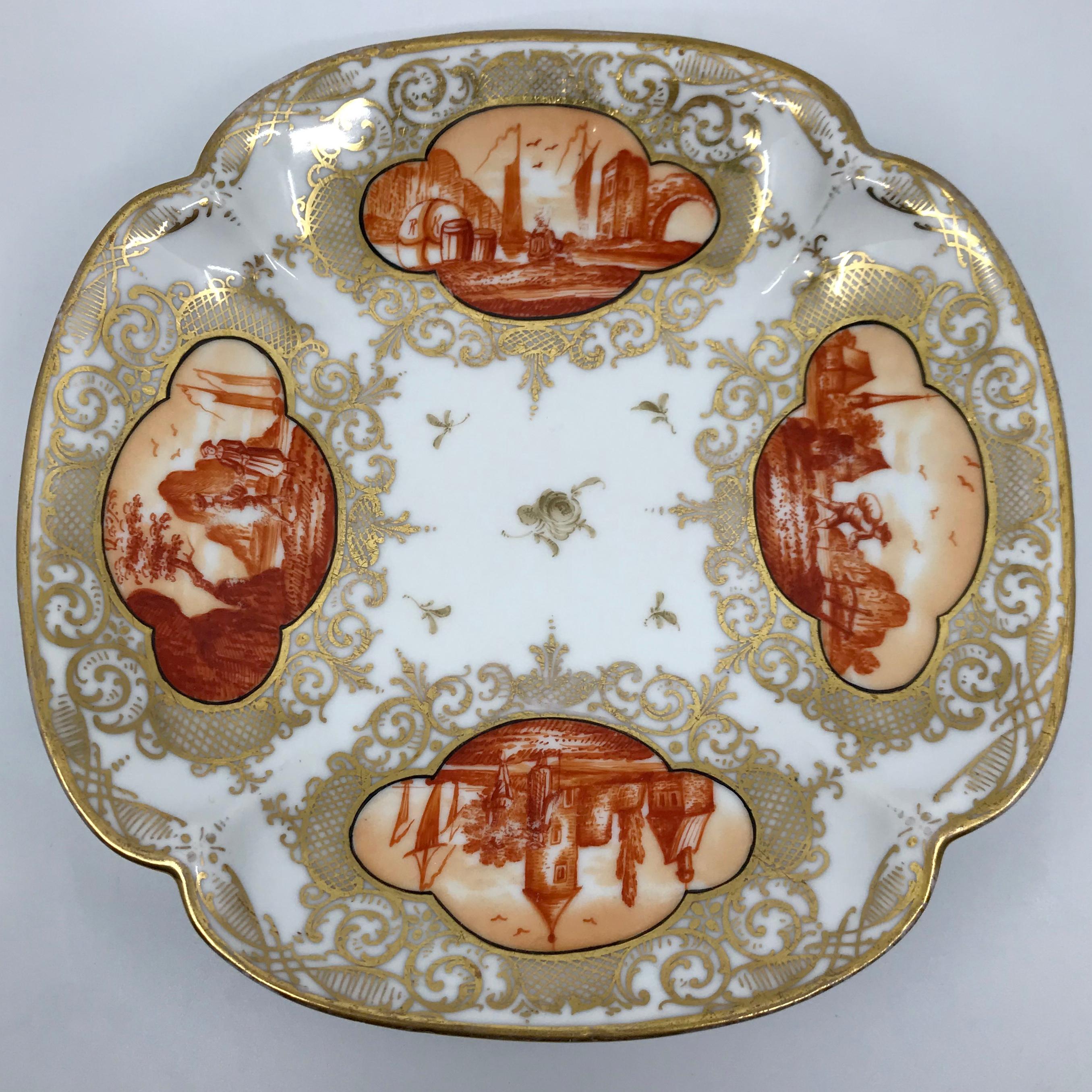 Set of four orange and gilt painted plates. Set of four shaped and painted plates with iron red/orange painted scenes of Continental harbours, castles and landmarks with gilt surrounds. Underglaze markings in blue for Dresden. Germany, late 19th