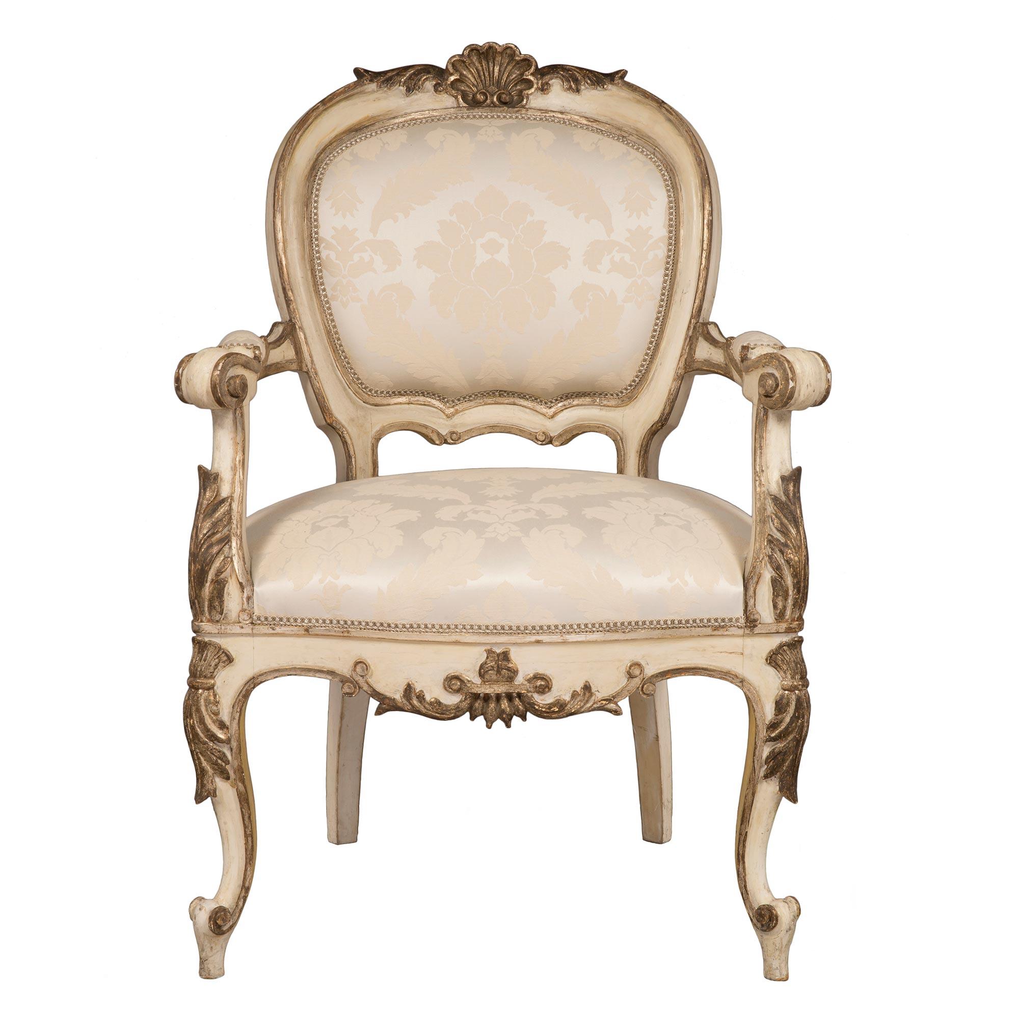 A very attractive set of four Italian early 19th century Louis XV st. patinated off white and Mecca armchairs. Each chair is raised by ‘S’ scrolled cabriole legs with large carved Mecca acanthus leaves at the top. The scalloped shaped frieze has a
