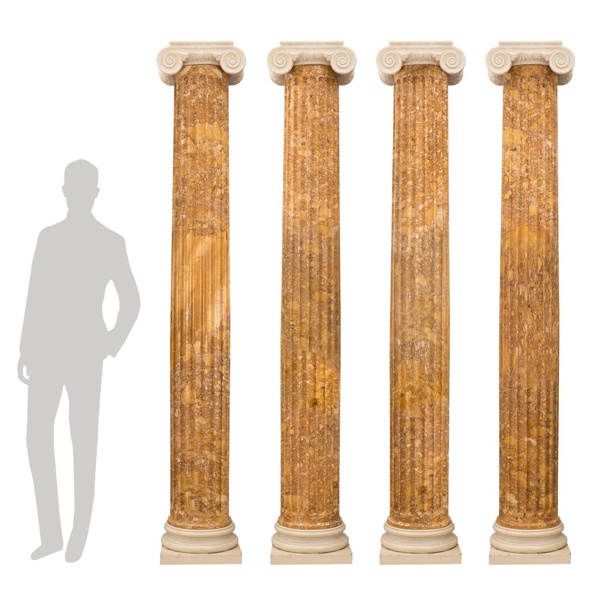 Un ensemble sensationnel et monumental de quatre colonnes ioniques architecturales italiennes de style Louis XVI du XIXe siècle en marbre de Sienne et de Carrare blanc. Chaque colonne à l'échelle palatiale est surélevée par une base carrée en marbre