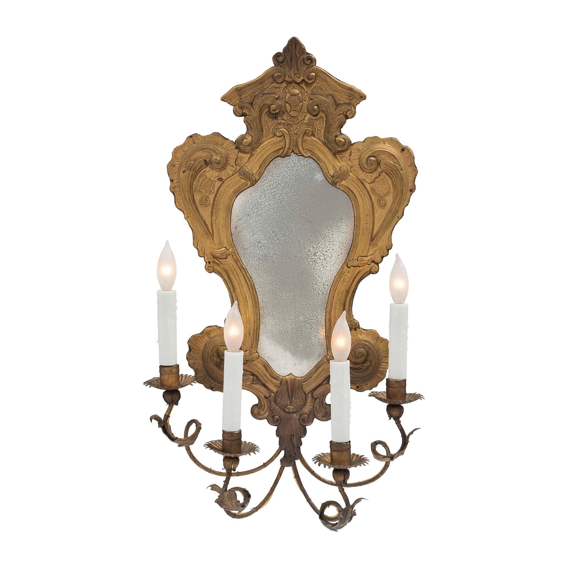 A very attractive and complete set of four Italian turn of the century Louis XV st. pressed brass mirrored sconces. Each sconce displays a top central crown with scrolls flanked by a serpentine shaped design surrounding a period mirror plate. The