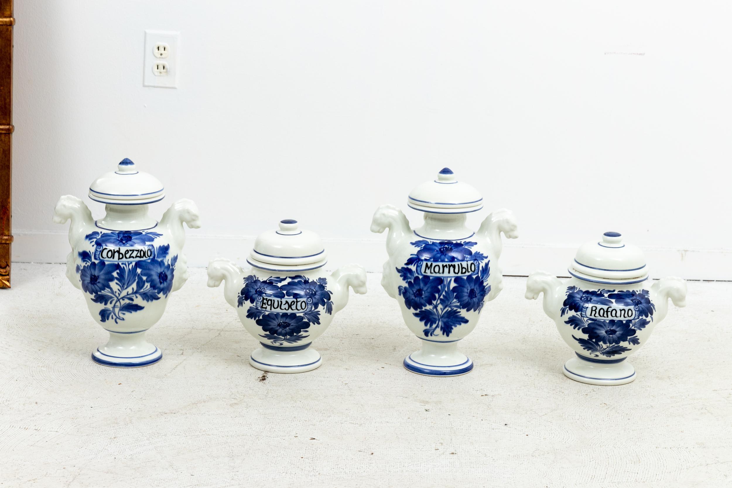 Set of four Italian painted apothecary jars painted in blue and white with handles, Circa 20th century. The jars also feature floral patterns and black painted lettering. Please note of wear consistent with age and use.