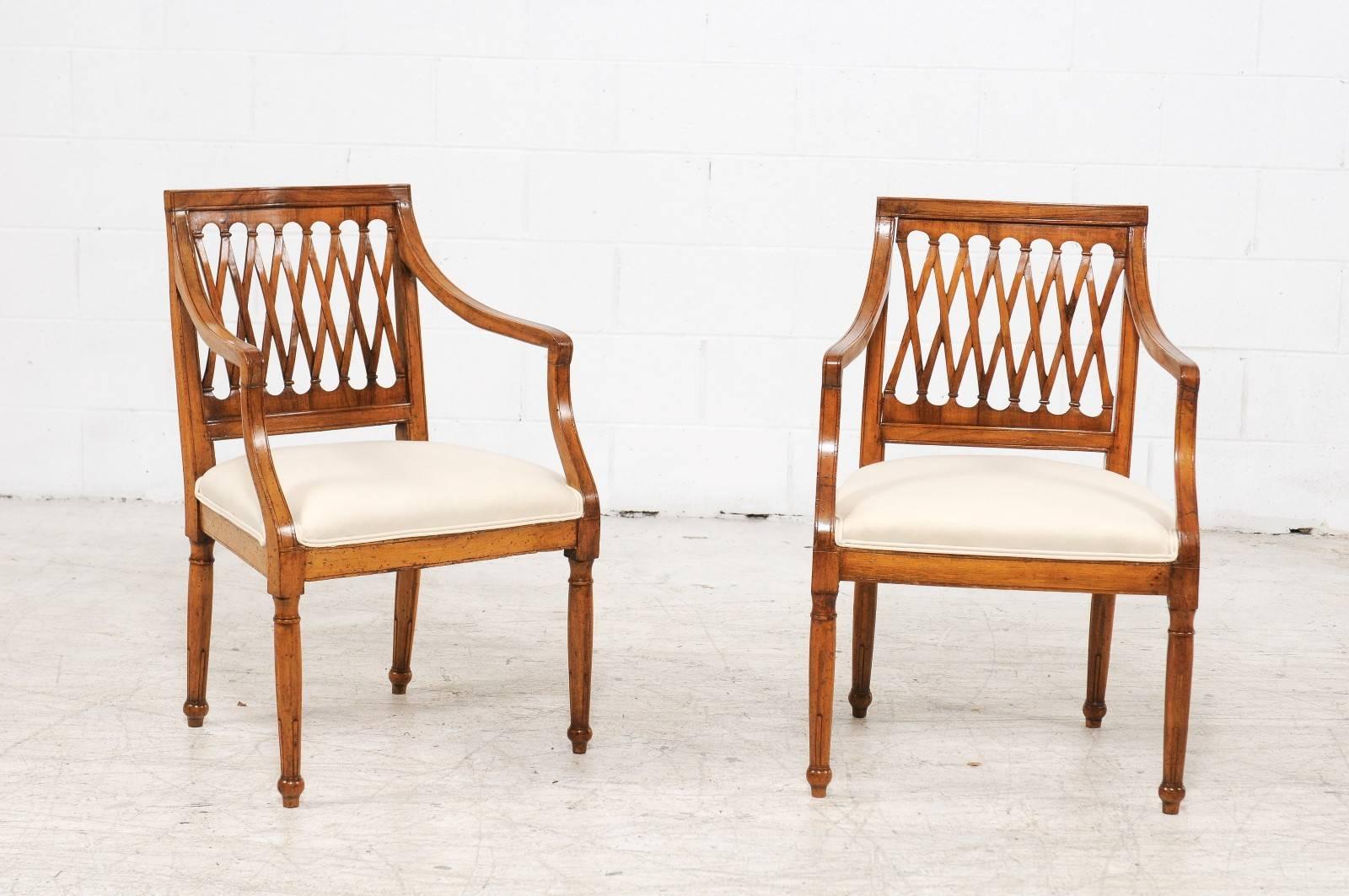 A set of four vintage Italian dining room armchairs with latticed backs, scrolled arms, upholstered seats and cylindrical legs from the first half of the 20th century. Each of this set of Italian chairs features an unusual latticed back flanked with