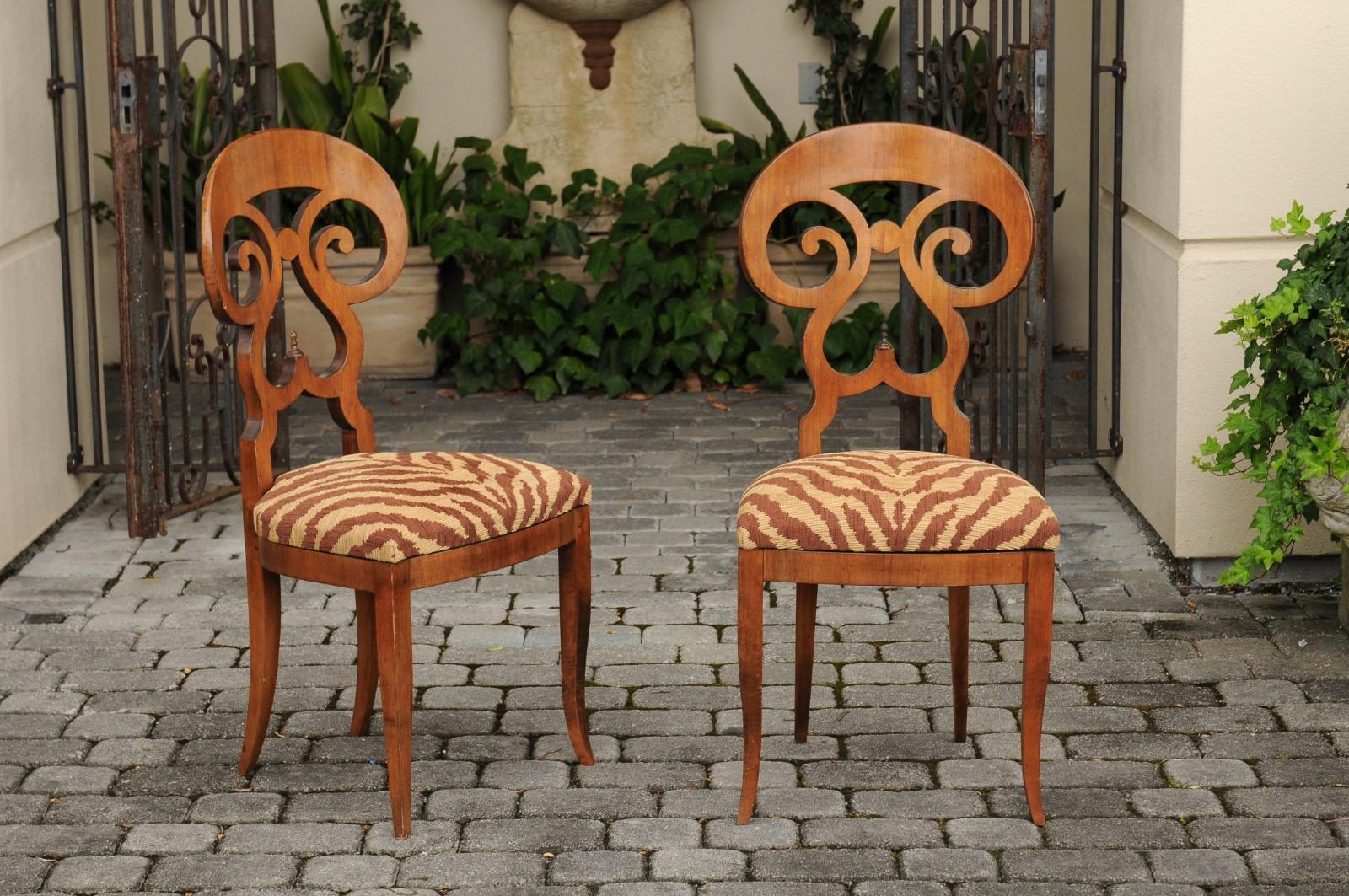 A set of four Italian walnut dining room side chairs from the early 20th century, with carved backs and animal print fabrics. Born in Italy during the early years of the 20th century, each of this set of side chairs features an elegant back, with