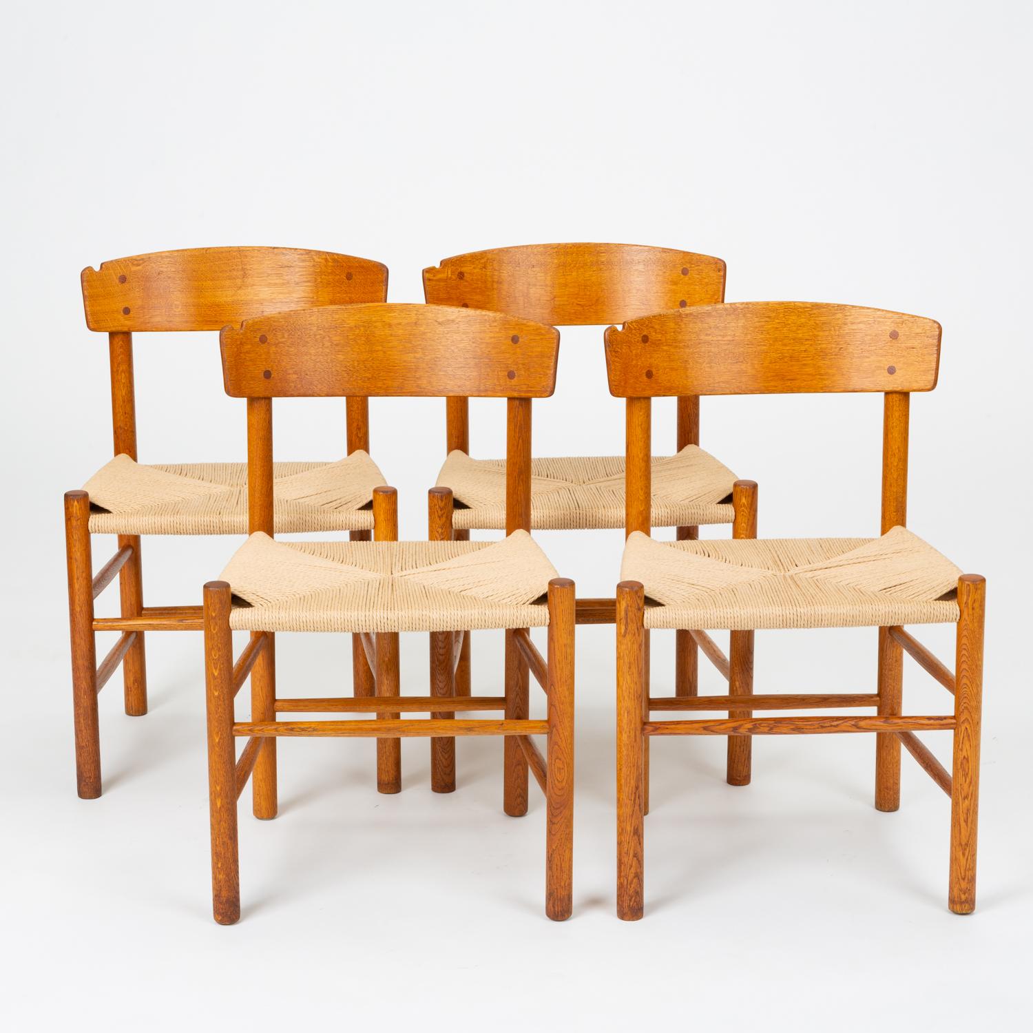A set of four customized dining chairs by Børge Mogensen for FDB Møbler beginning in 1947. The J39 or “People’s Chair,” has a frame of oak dowels, with a wide, curved backrest and a woven seat in Danish paper cord. Each backrest has a smooth notch