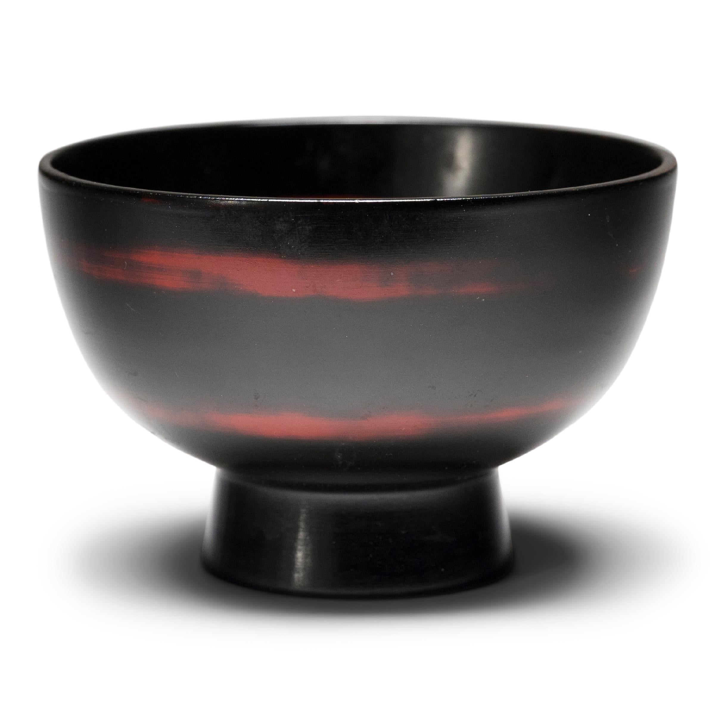 This set of four lacquered rice bowls is simply shaped with gently tapered sides and a footed base. A rich, glossy black finish coats the bowls inside and out, with a contrasting red lacquer spiral detailing on each bowl. Lightweight and compact,