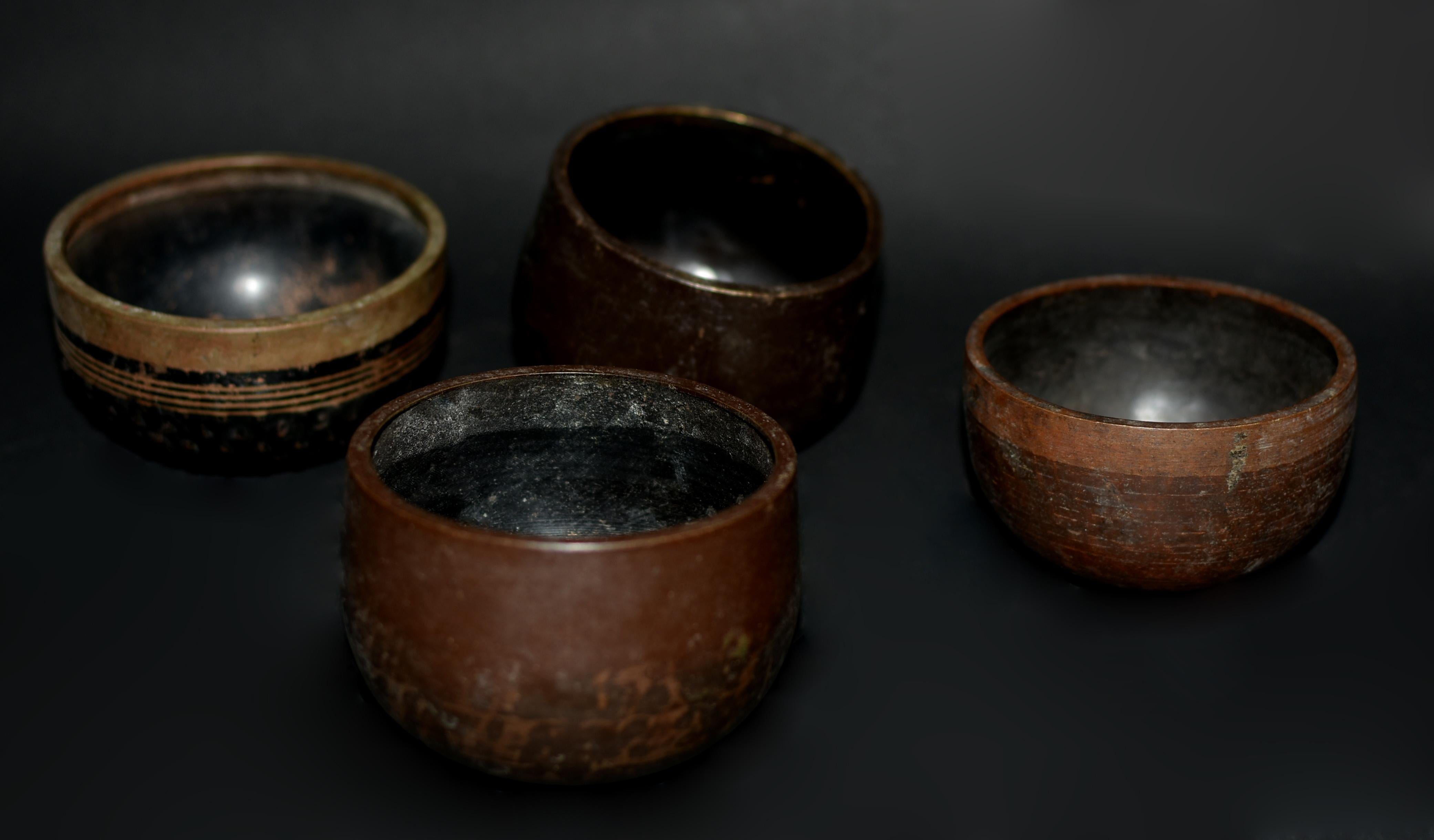 A set of four small 20th century solid bronze Japanese singing bowls. Included are four unique pieces, one a chocolate brown bowl with wide band, one dark espresso bronze piece, a black bronze upright bowl and a black bowl with gold rings and raised